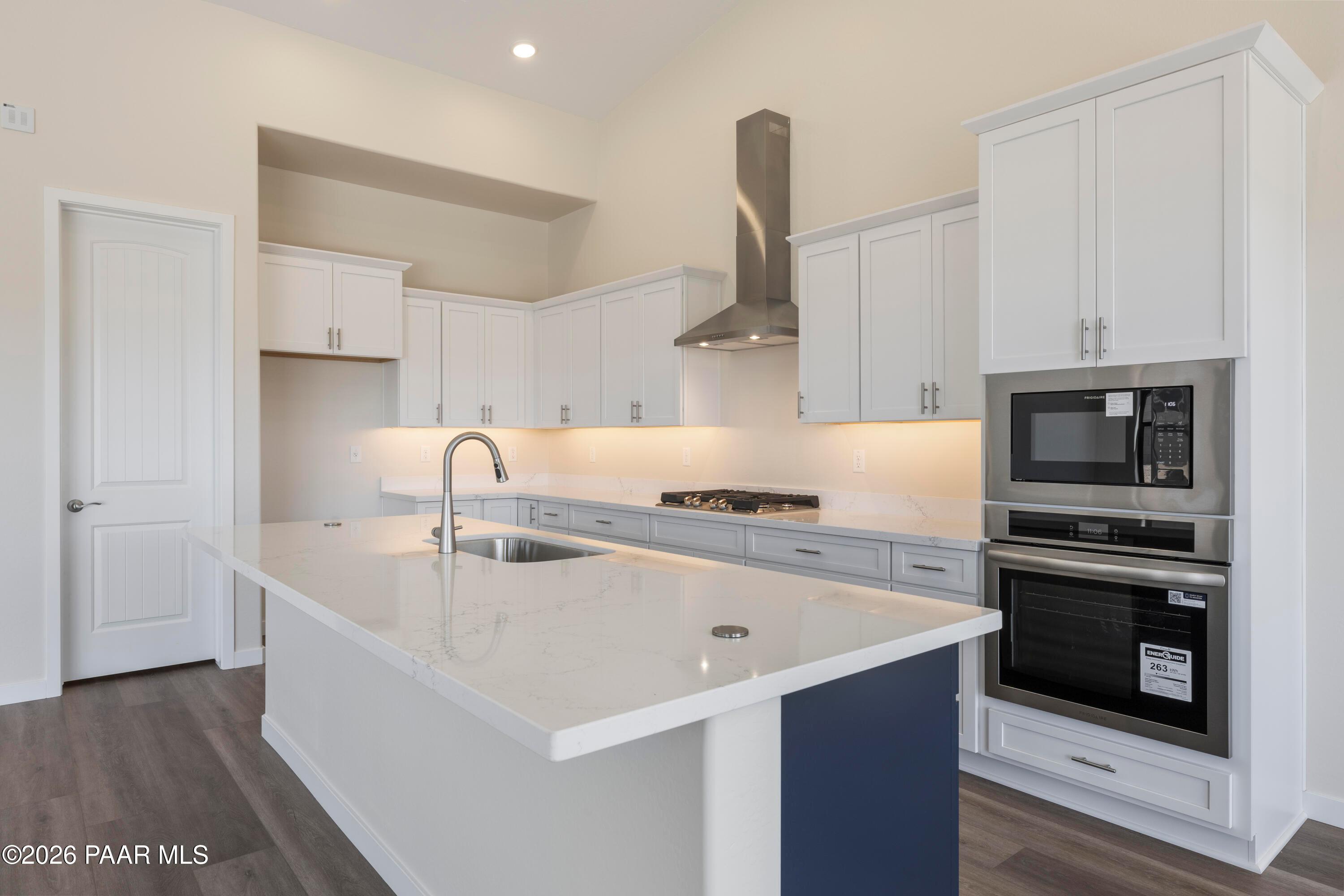 Modern white kitchen with quartz island, stainless appliances, and range hood in Davidson Homes Soleil E, Prescott AZ