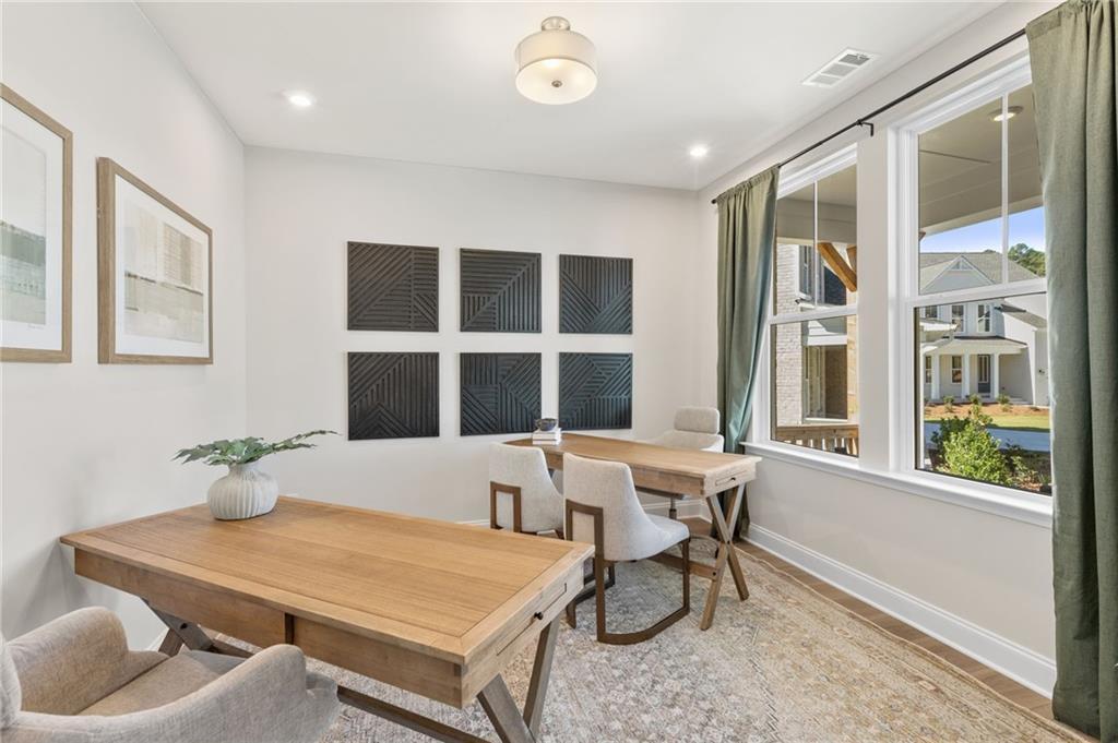 Bright home office with dual wooden desks, large windows overlooking backyard, and abstract wall art in Davidson Homes Danbury C, Buford, GA