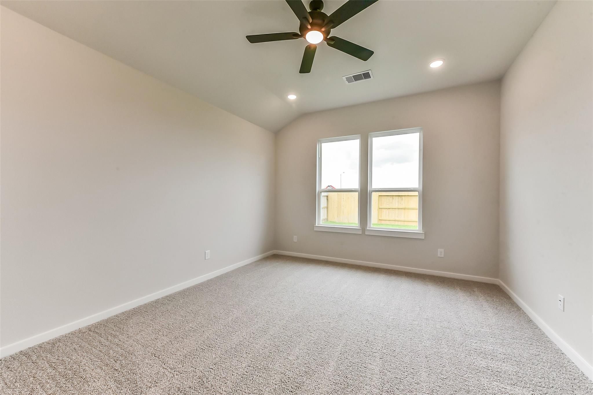 Spacious empty bedroom with vaulted ceiling, ceiling fan, beige carpet, and large windows overlooking backyard in The Sequoia C, Crosby Texas