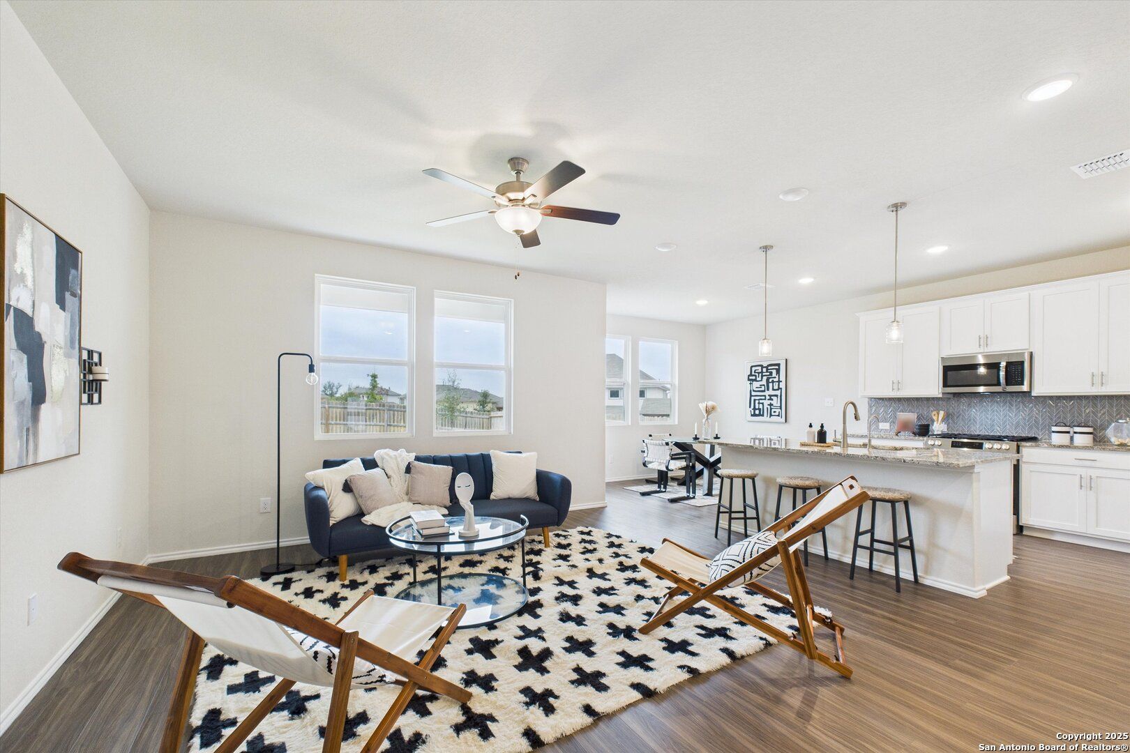 Open-concept living room with navy sofa, patterned rug, armchairs, and adjacent white kitchen island in Asheville K home, San Antonio