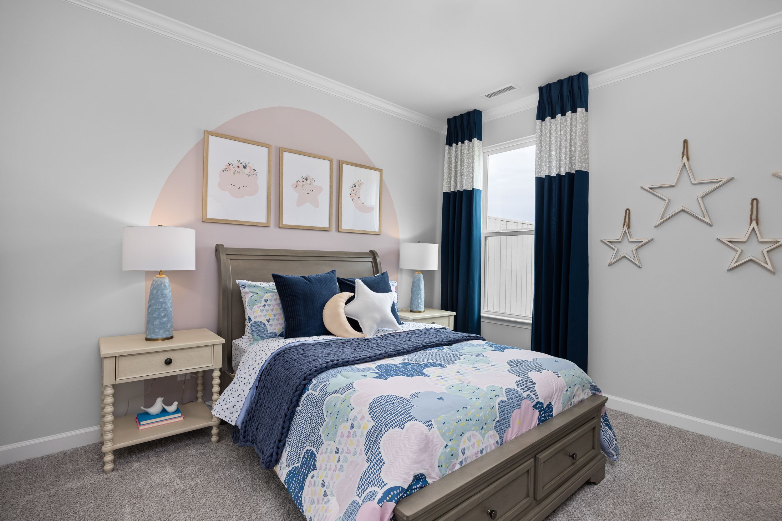 Whimsical bedroom in The Magnolia B with cloud duvet, navy pillows, arched pink art, blue curtains, and star accents