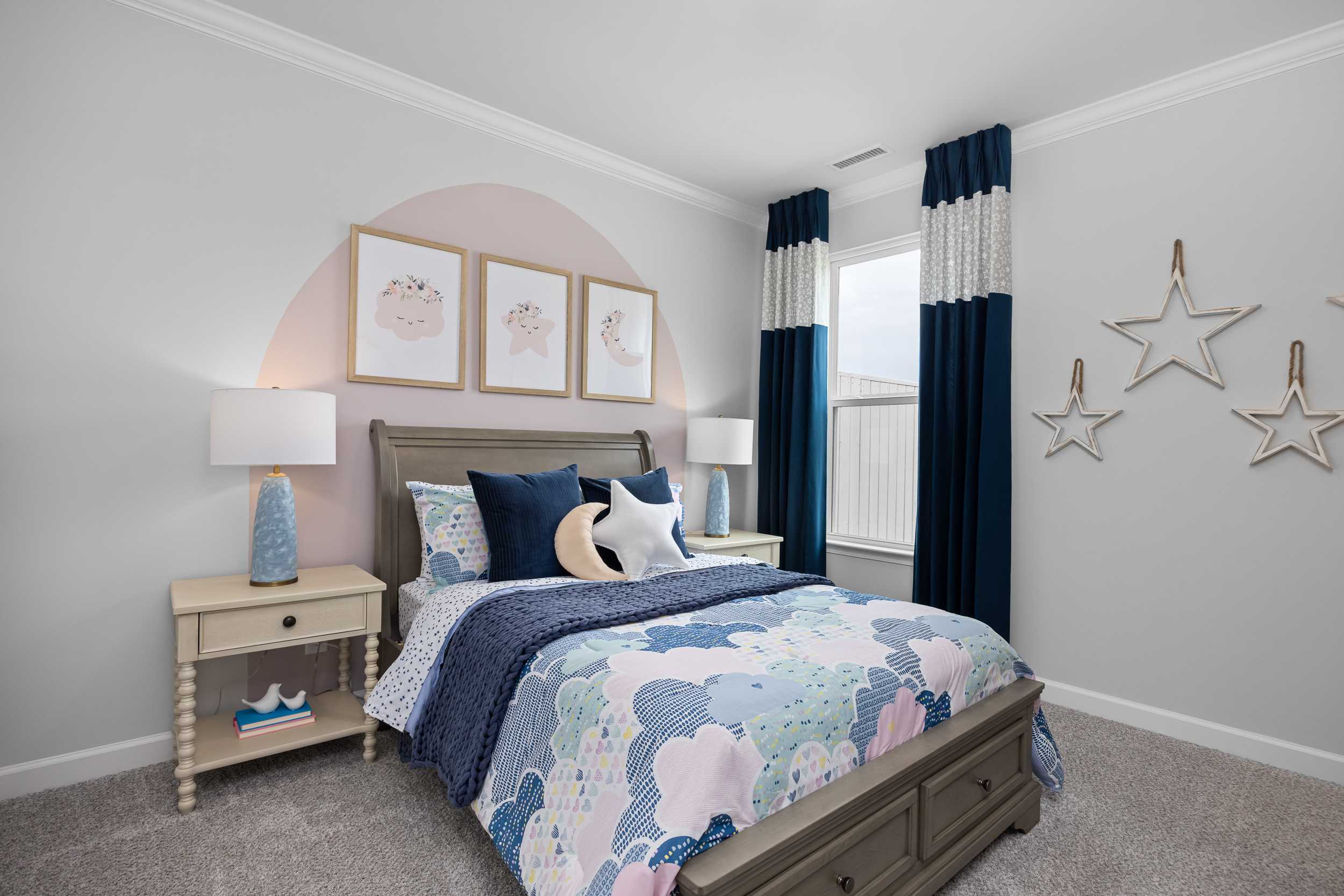 Whimsical child's bedroom in The Magnolia A Davidson Homes design with cloud-patterned bed, navy star pillows, arched pink wall art