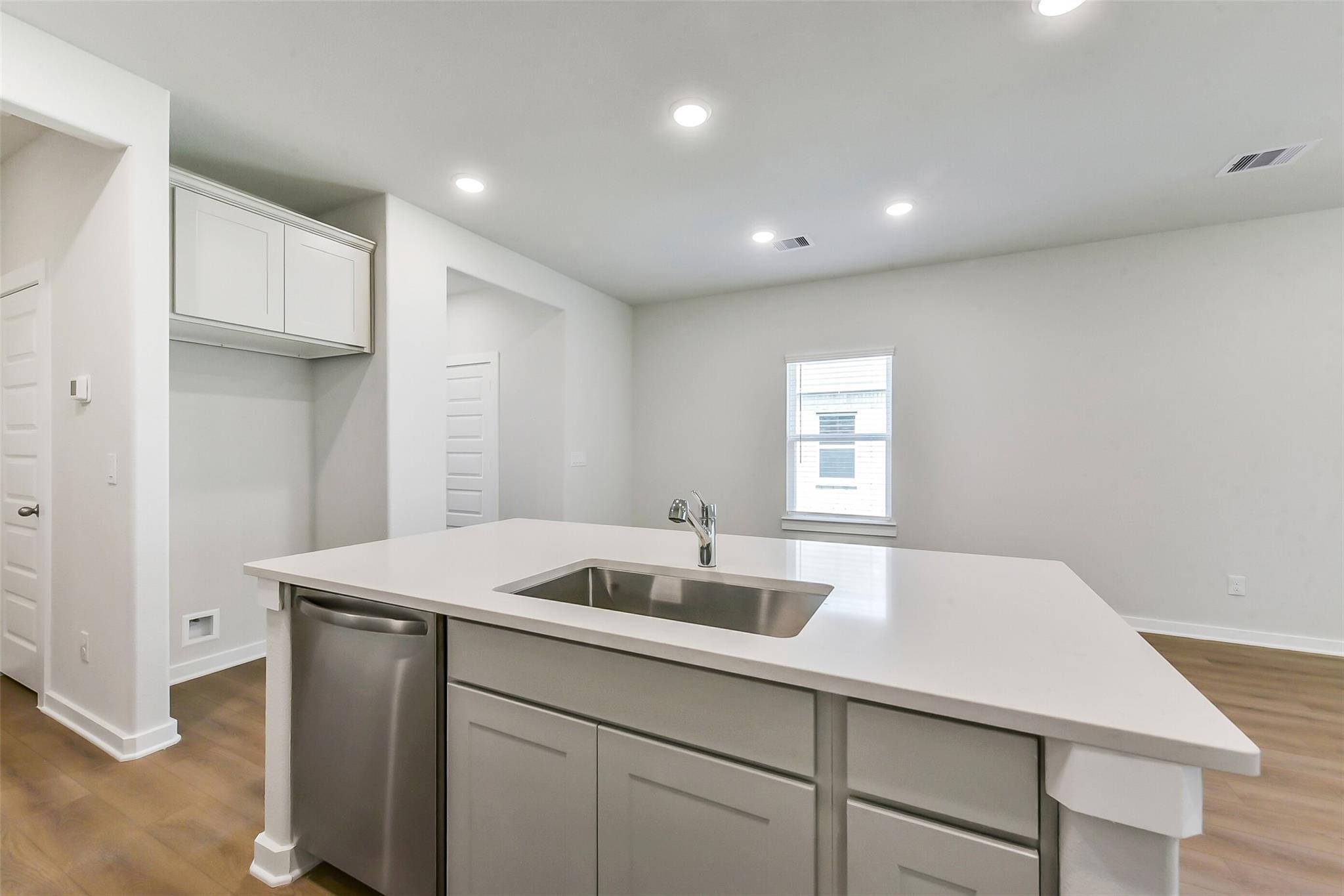 Modern white quartz kitchen island with stainless sink and dishwasher in Davidson Homes The Brazos E, Magnolia Texas
