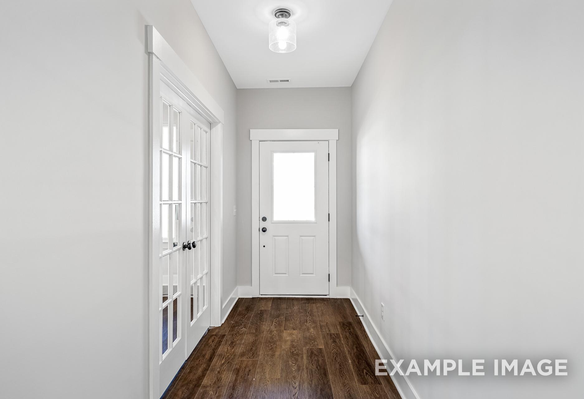 Bright hallway in The Henry A home with gray walls, hardwood floors, white French doors, and entry door