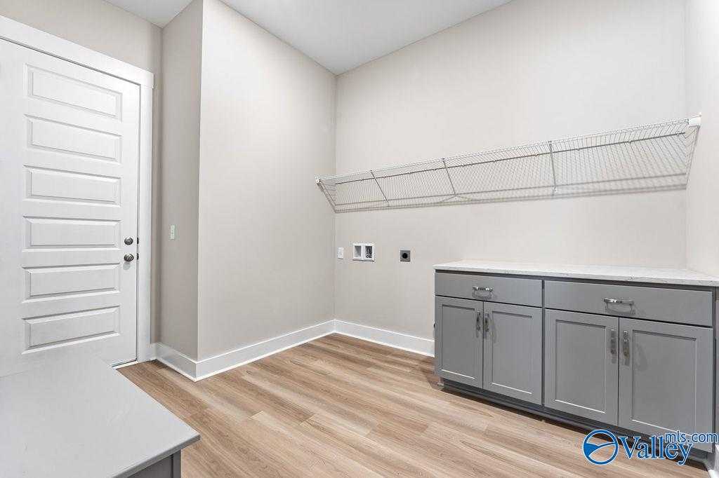 Functional laundry room featuring gray cabinets, wire shelving, washer/dryer hookups and LVP flooring in Evermore Homes The Oxford, Owens Cross Roads, AL