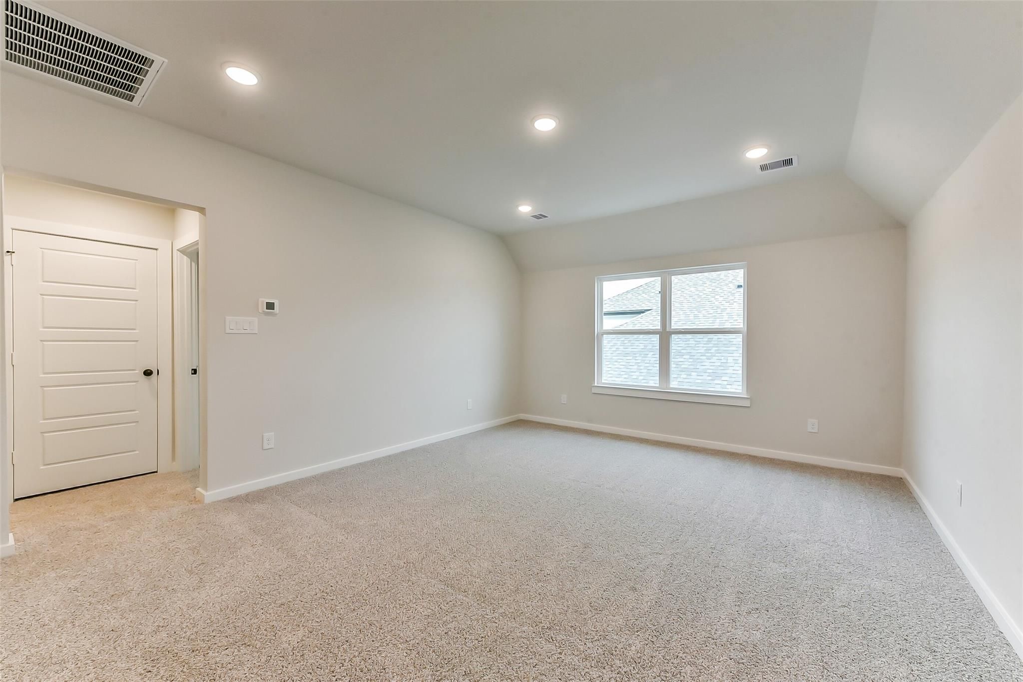 Spacious empty bedroom with beige carpet, vaulted ceiling, large divided-light window, and recessed lighting in Davidson Homes Sequoia C, Crosby Texas
