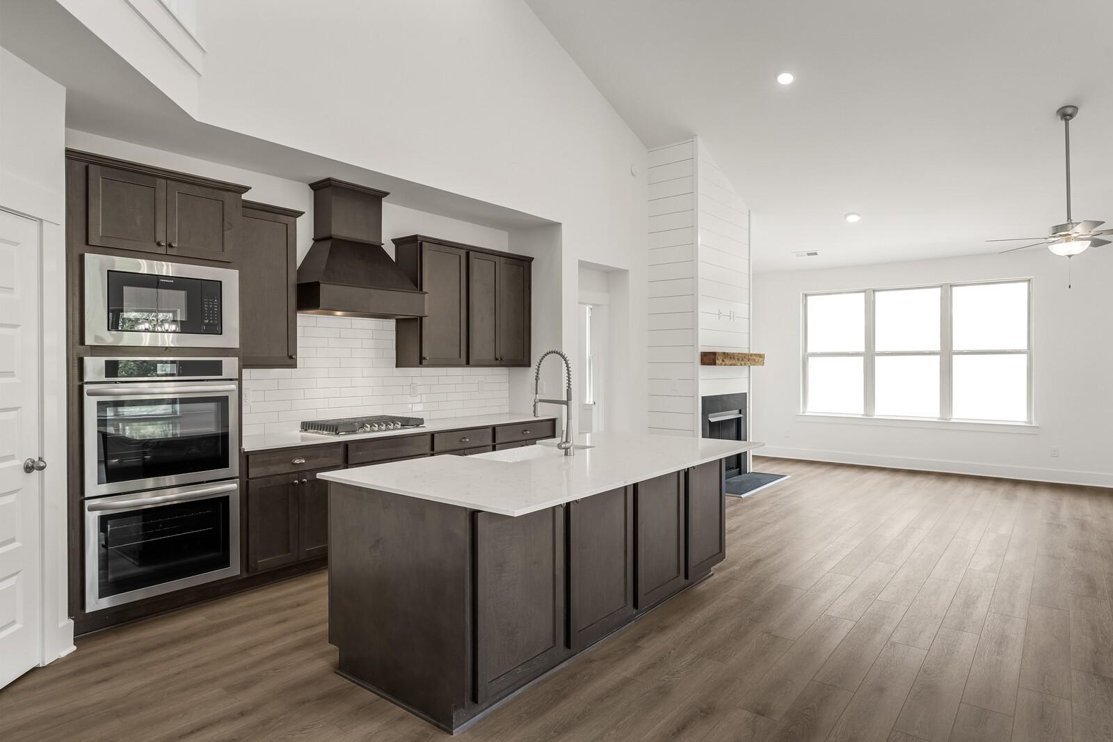Open-concept kitchen with dark cabinets and quartz island in The Ridgeport C floor plan at Woods Crossing, Gallatin.