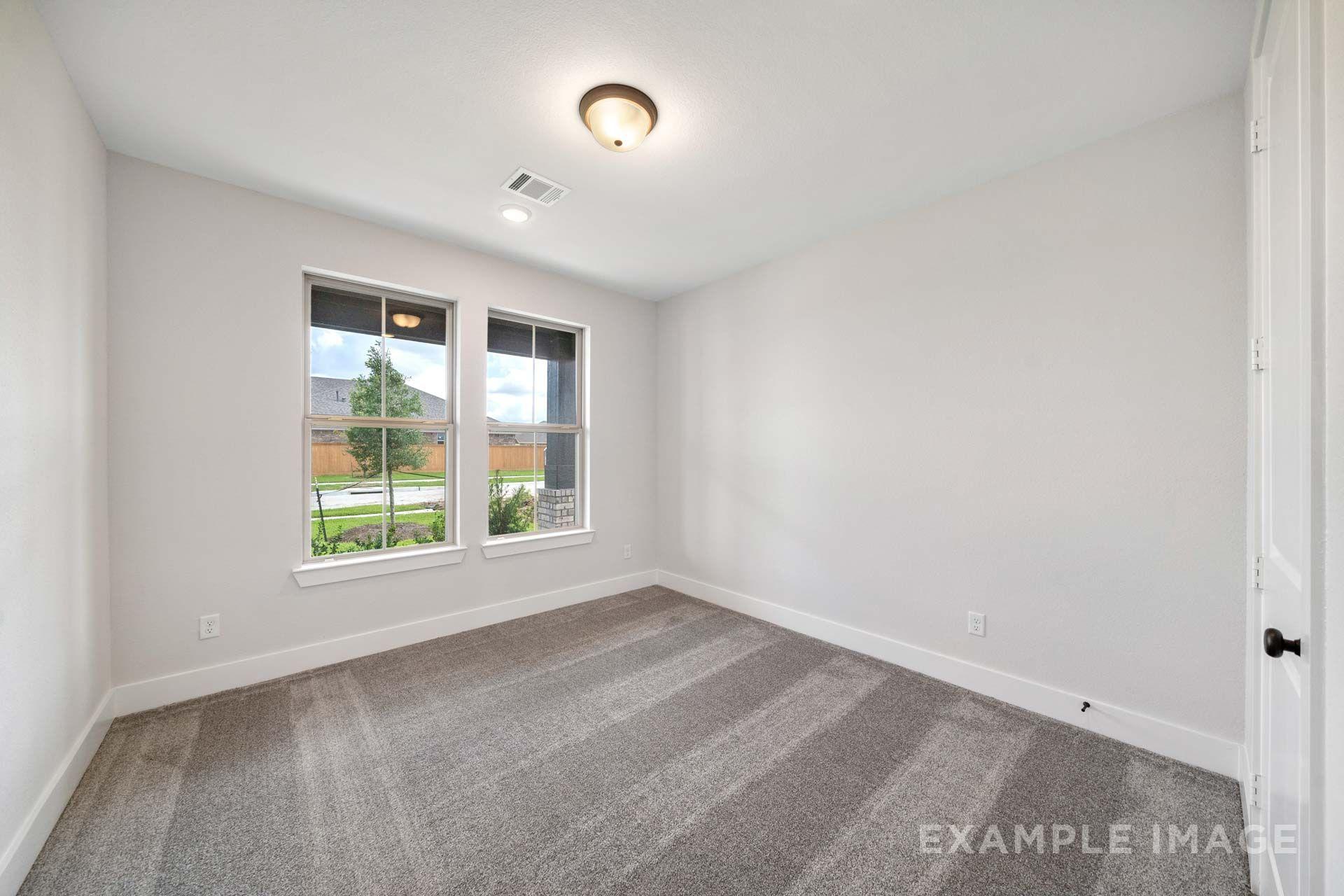 Spacious carpeted bedroom in The Victoria by Davidson Homes, featuring white walls, dual windows, and natural light in Texas City.