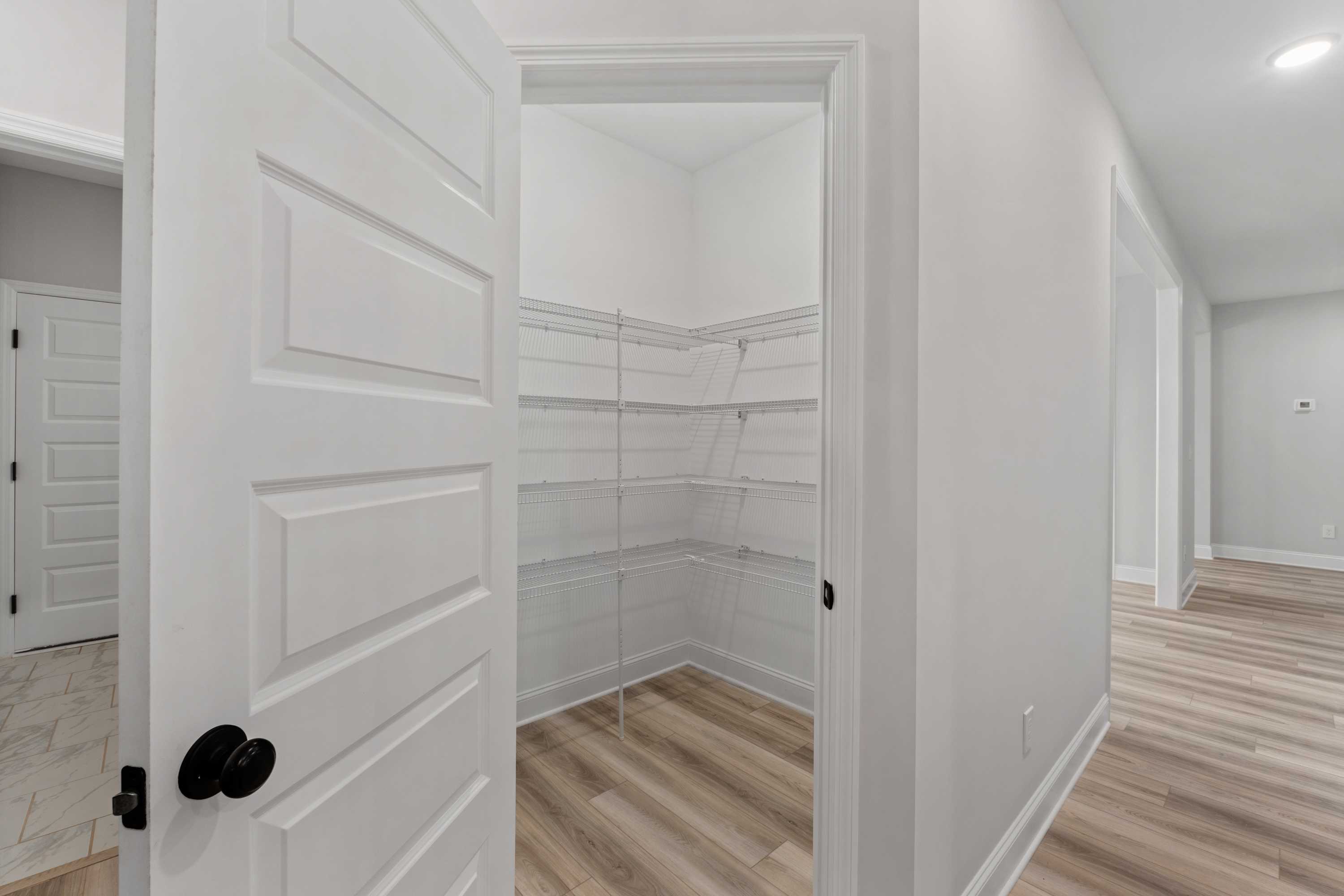 Spacious walk-in closet in The Oxford floor plan with open white doors, wire shelving, and light wood laminate flooring