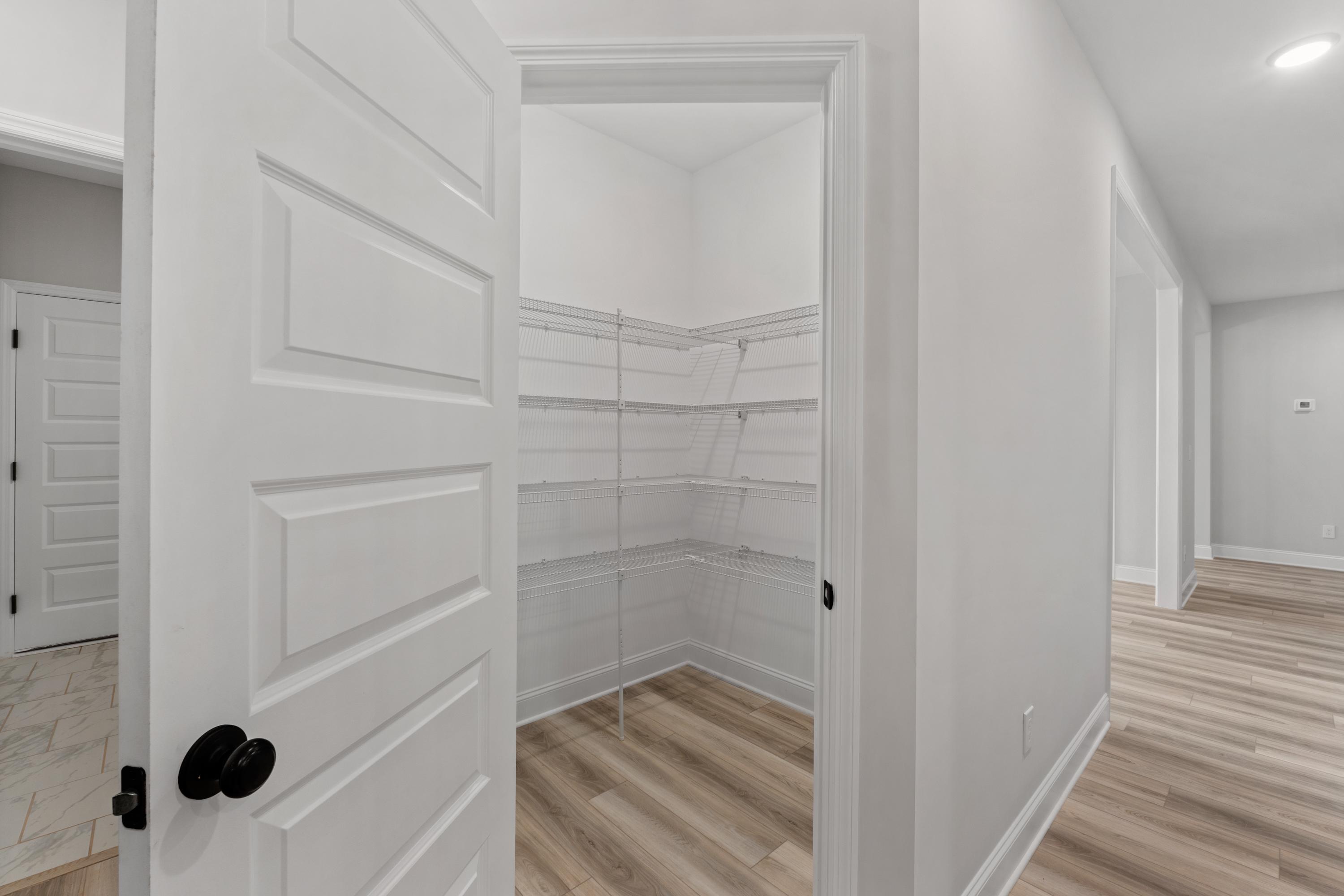 Spacious walk-in closet in The Oxford floor plan with open white doors, wire shelving, and light wood laminate flooring