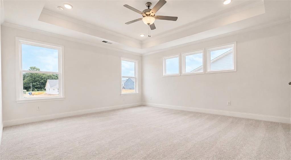 Spacious master bedroom with tray ceiling and ceiling fan in The Hickory C floor plan at Wehunt Meadows, Hoschton, GA.