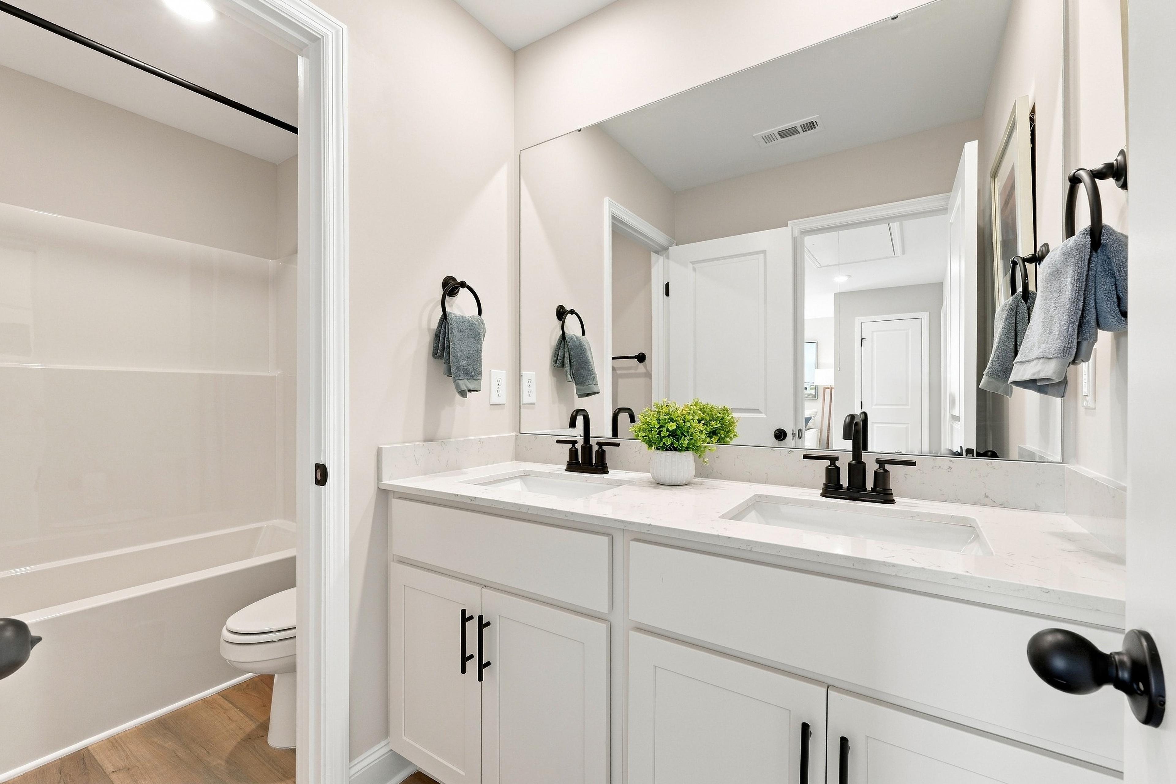 White double vanity bathroom with black fixtures and tile shower at Bailey Park by Davidson Homes in Fayetteville, Tennessee