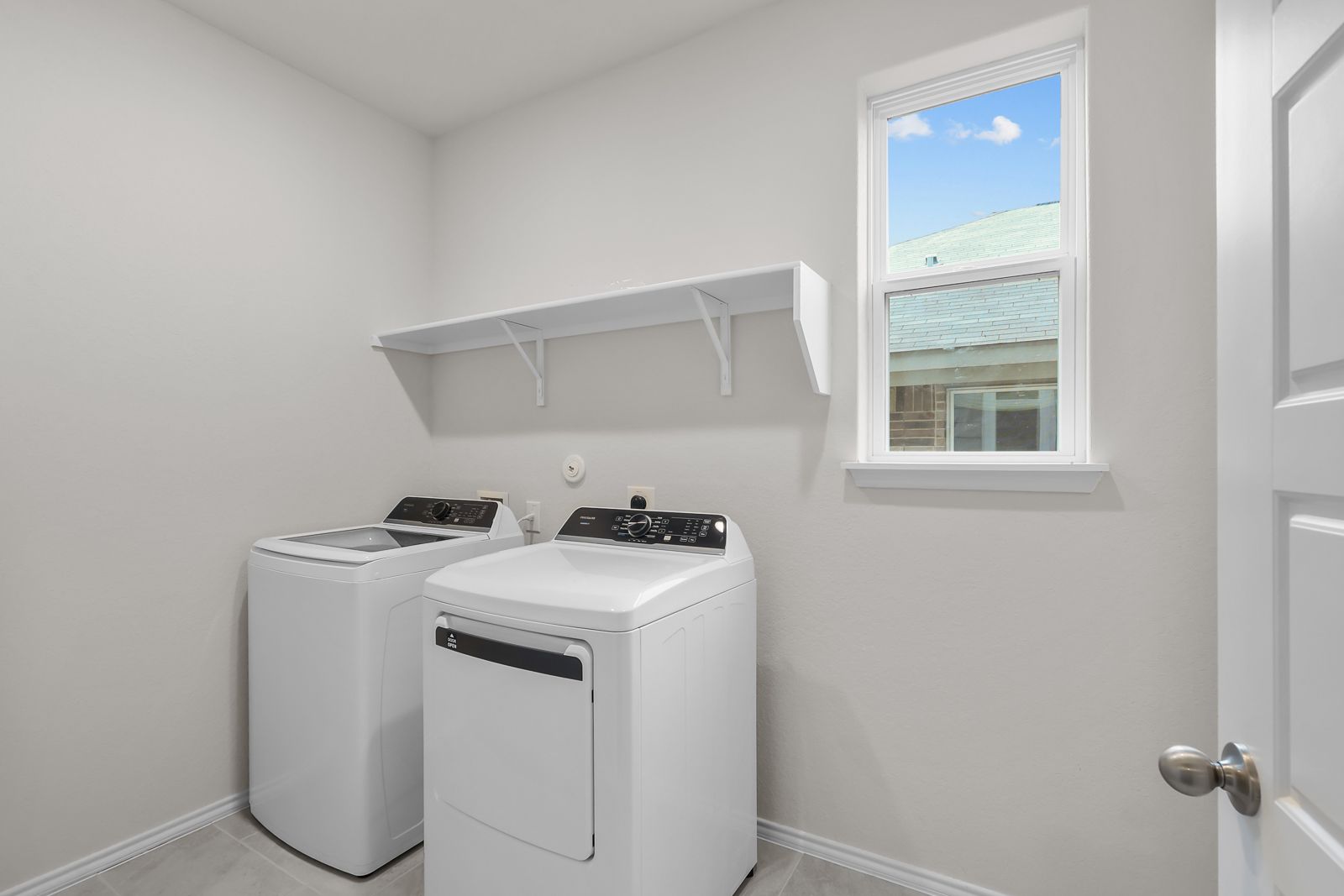 Bright laundry room in The Sequoia C featuring white washer and dryer, shelving, and a window for natural light.