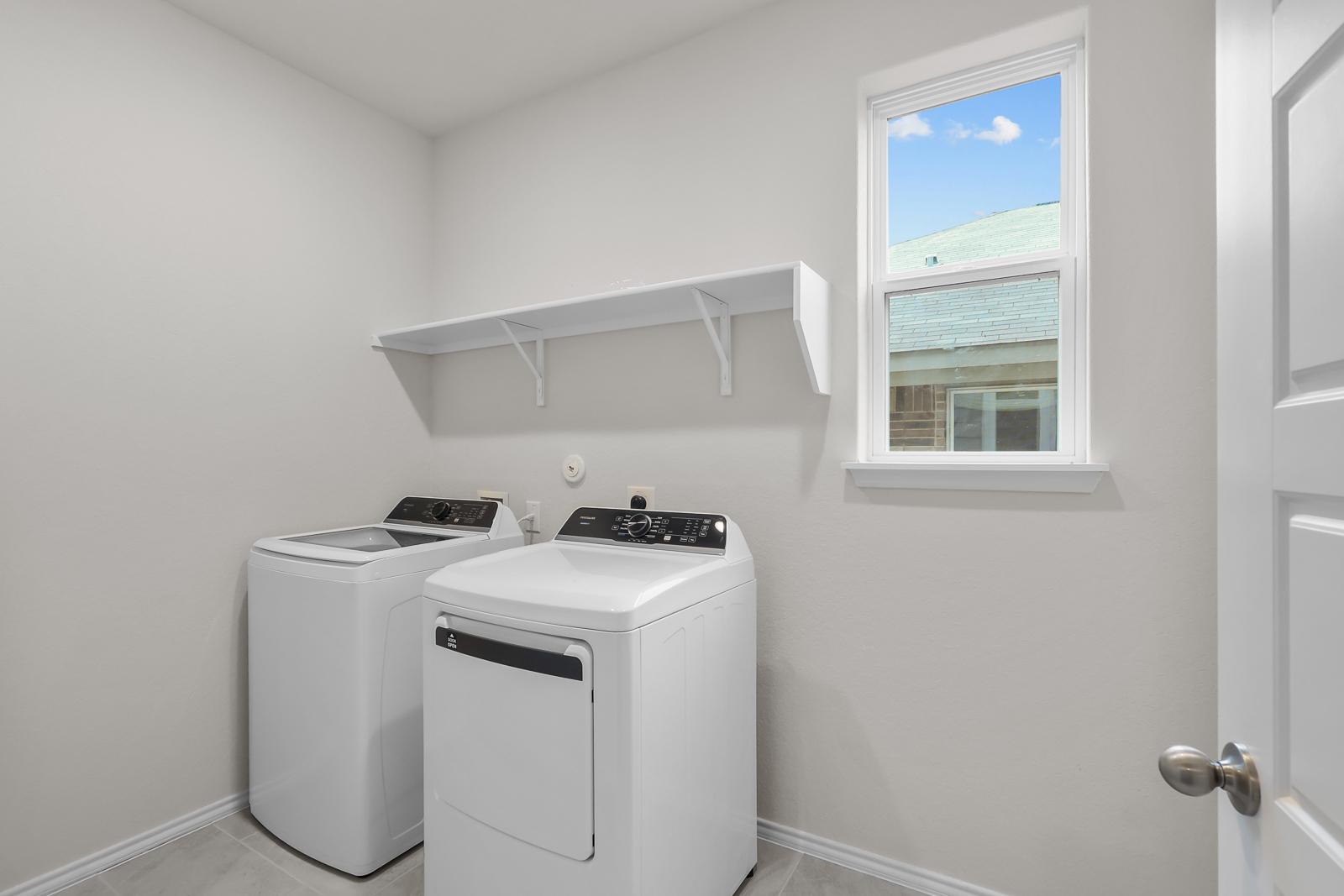 Bright laundry room in The Sequoia C featuring white washer and dryer, shelving, and a window for natural light.