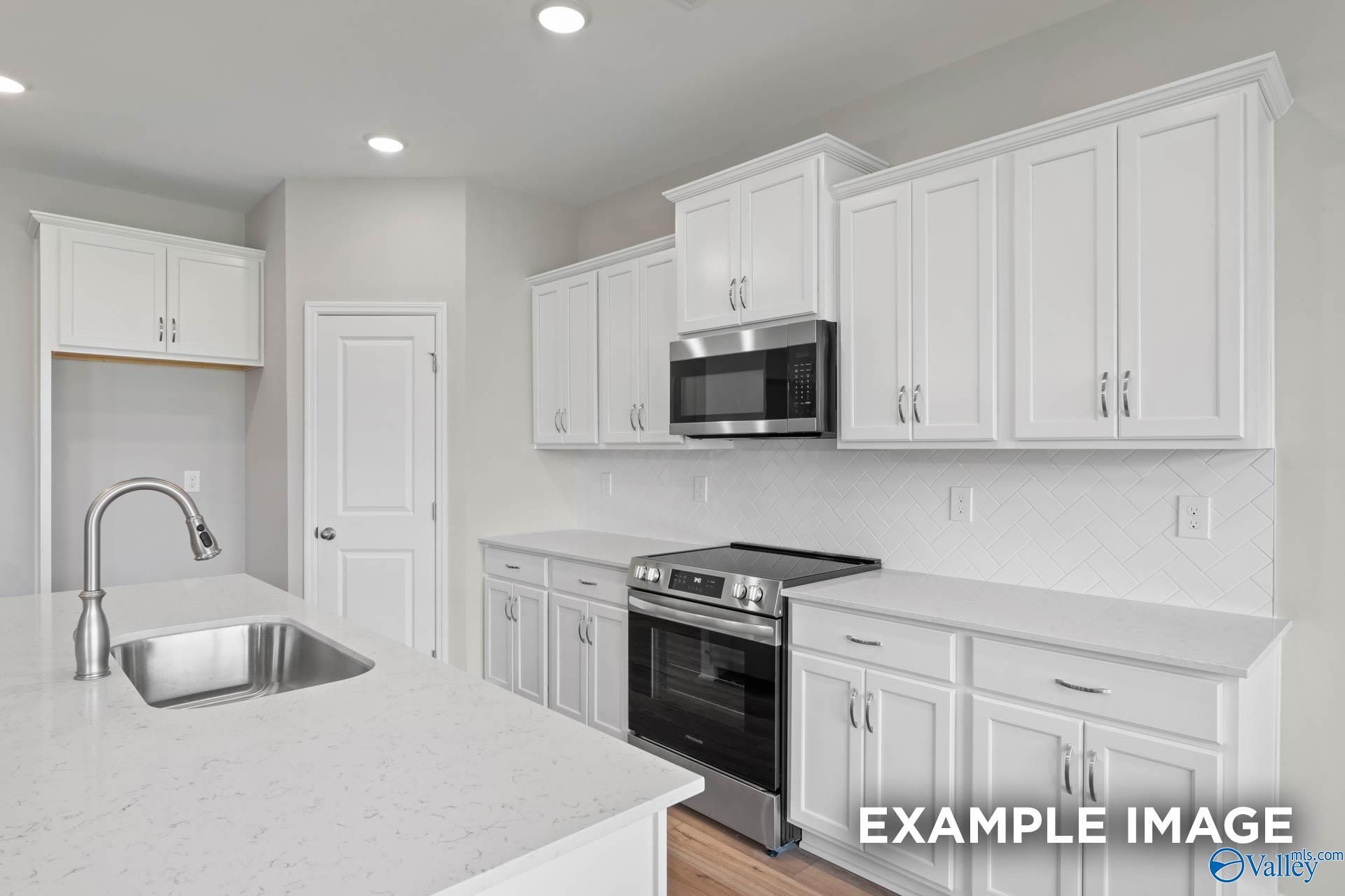 Bright modern kitchen with white shaker cabinets, stainless steel appliances, quartz island in Davidson Homes The Montgomery B, Hartselle AL