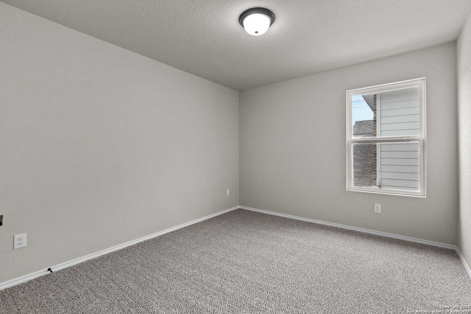 Bright empty bedroom with neutral gray walls, plush carpet, and window in Davidson Homes The Murray I, San Antonio, Texas