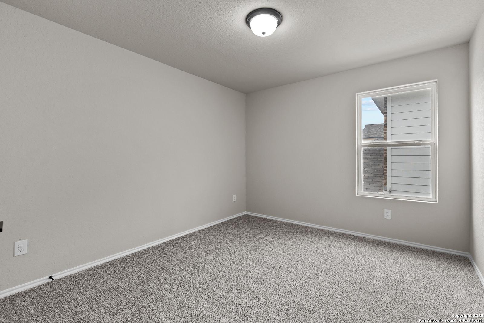 Bright empty bedroom with neutral gray walls, plush carpet, and window in Davidson Homes The Murray I, San Antonio, Texas
