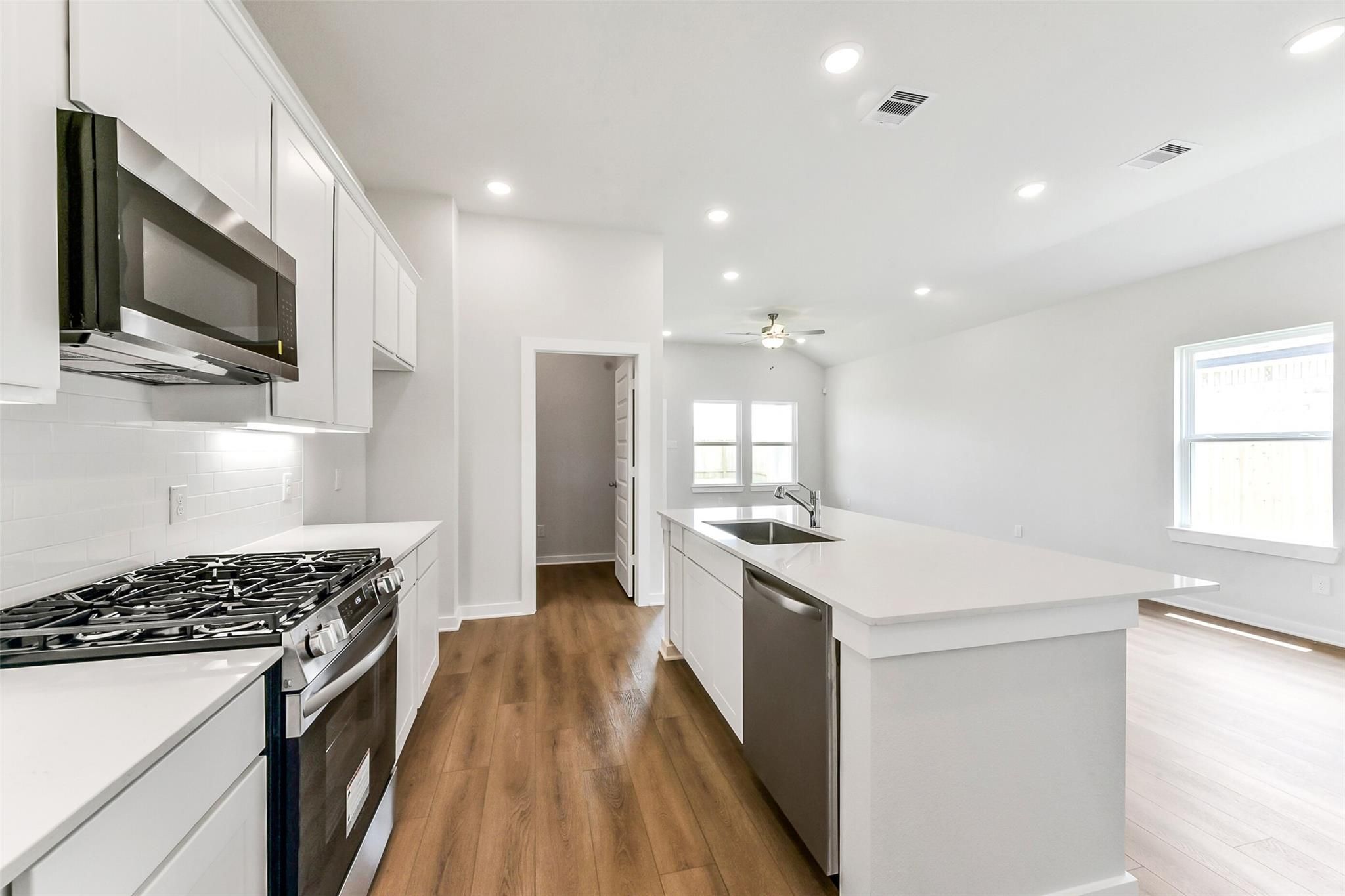 Modern white kitchen with stainless appliances, large island sink, and open layout in Davidson Homes The Costa B, Dayton, Texas