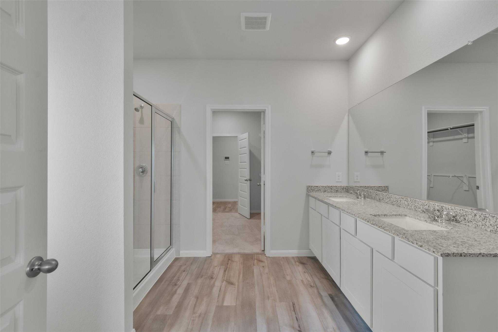 Modern master bathroom featuring double vanity with granite counters, walk-in shower, and wood flooring in Davidson Homes The Tierra A, Dayton, Texas