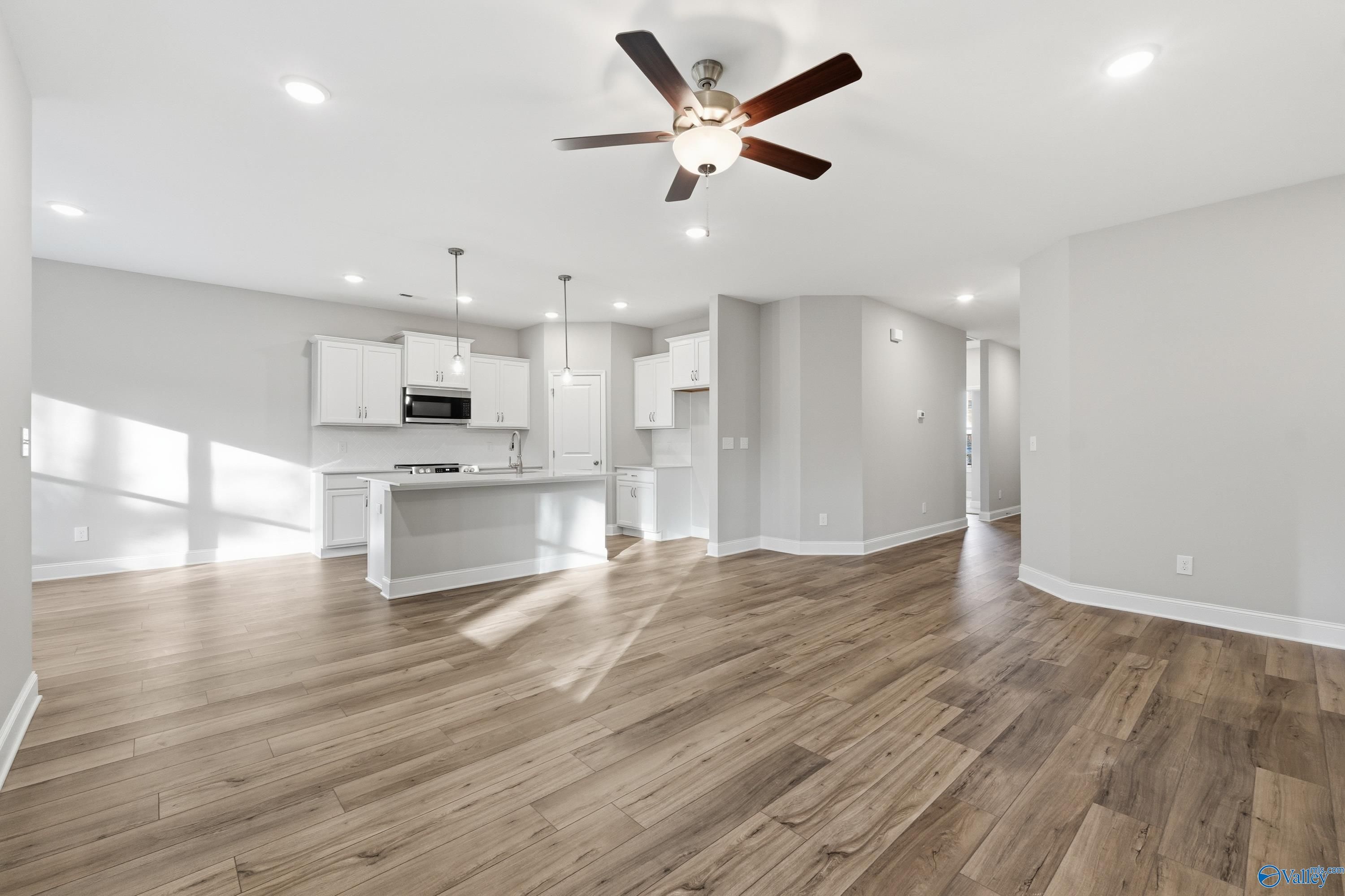 Open-concept kitchen-living area with white cabinets, hardwood floors, ceiling fan in The Asheville floor plan by Davidson Homes, Arab, AL