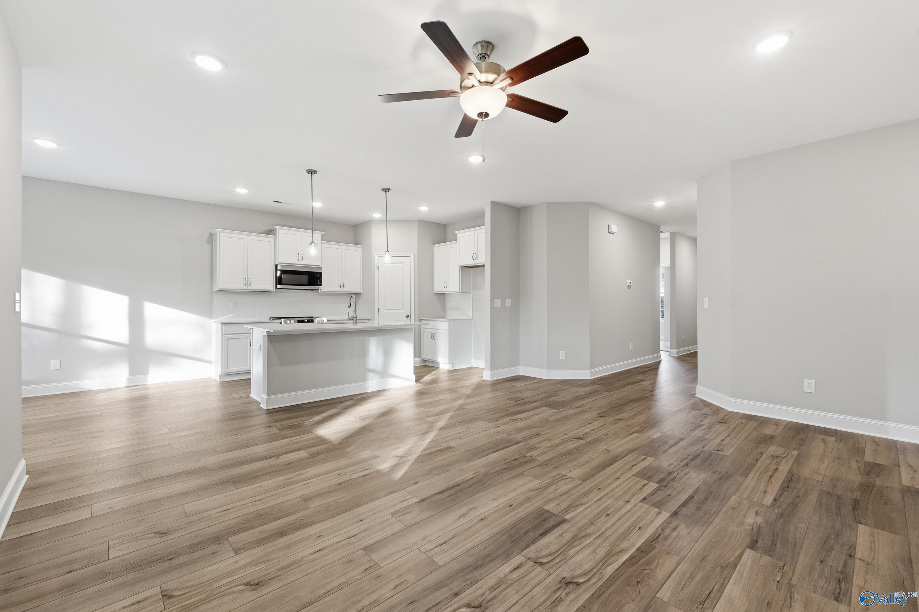 Open-concept kitchen-living area with white cabinets, hardwood floors, ceiling fan in The Asheville floor plan by Davidson Homes, Arab, AL