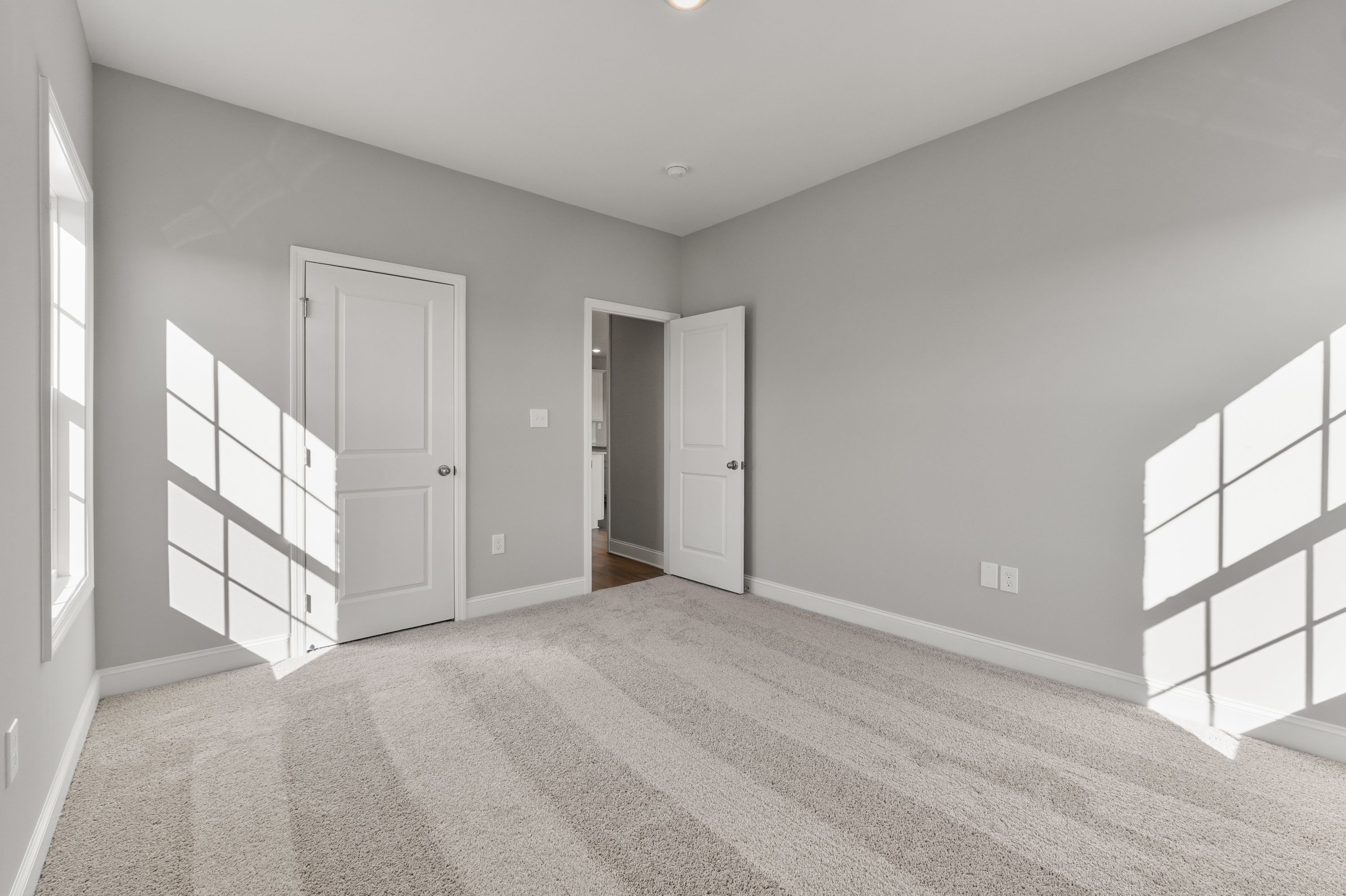 Spacious bedroom in The Valencia home with gray walls, beige carpet, white doors, and sunlit windows