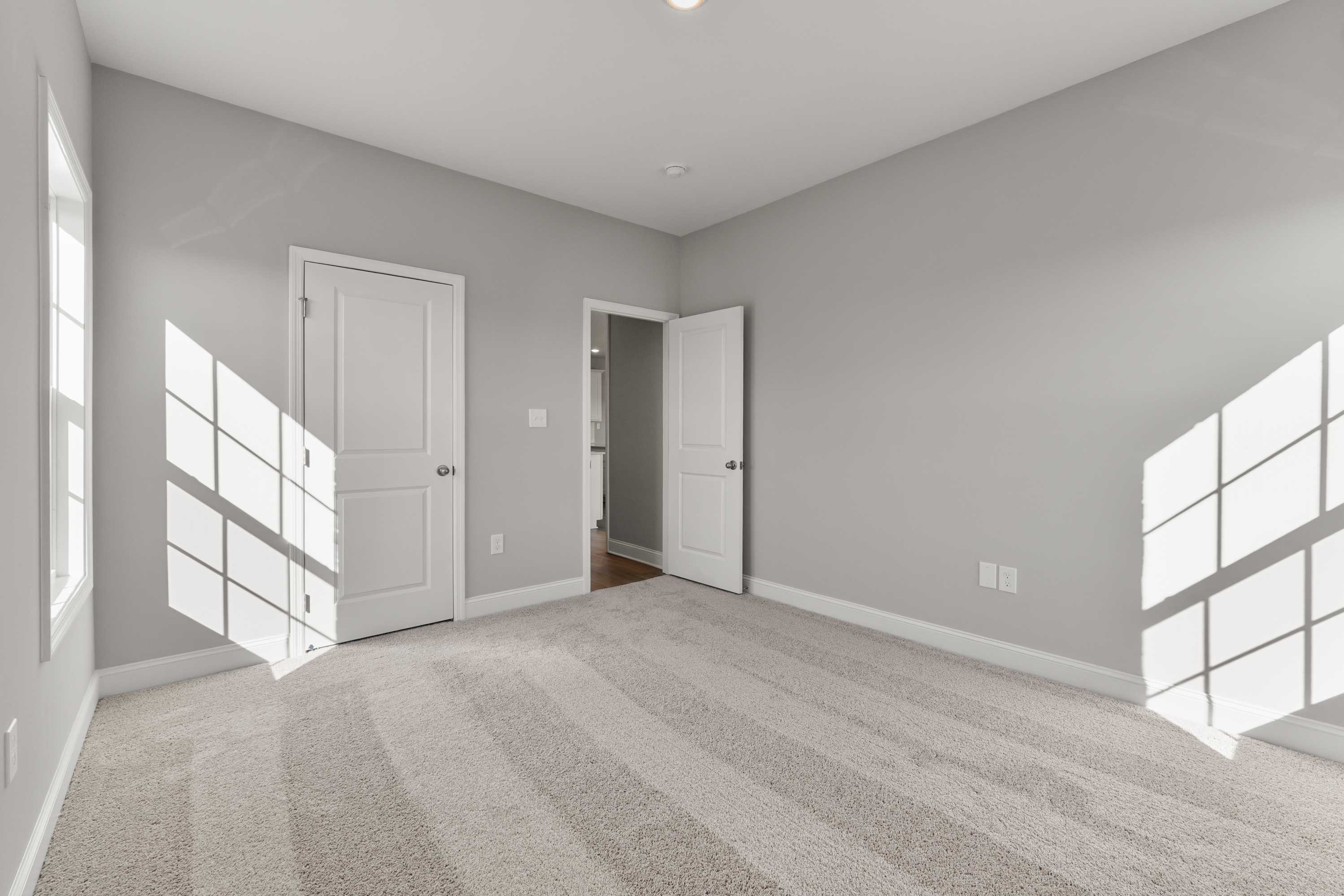 Spacious bedroom in The Valencia home with gray walls, beige carpet, white doors, and sunlit windows