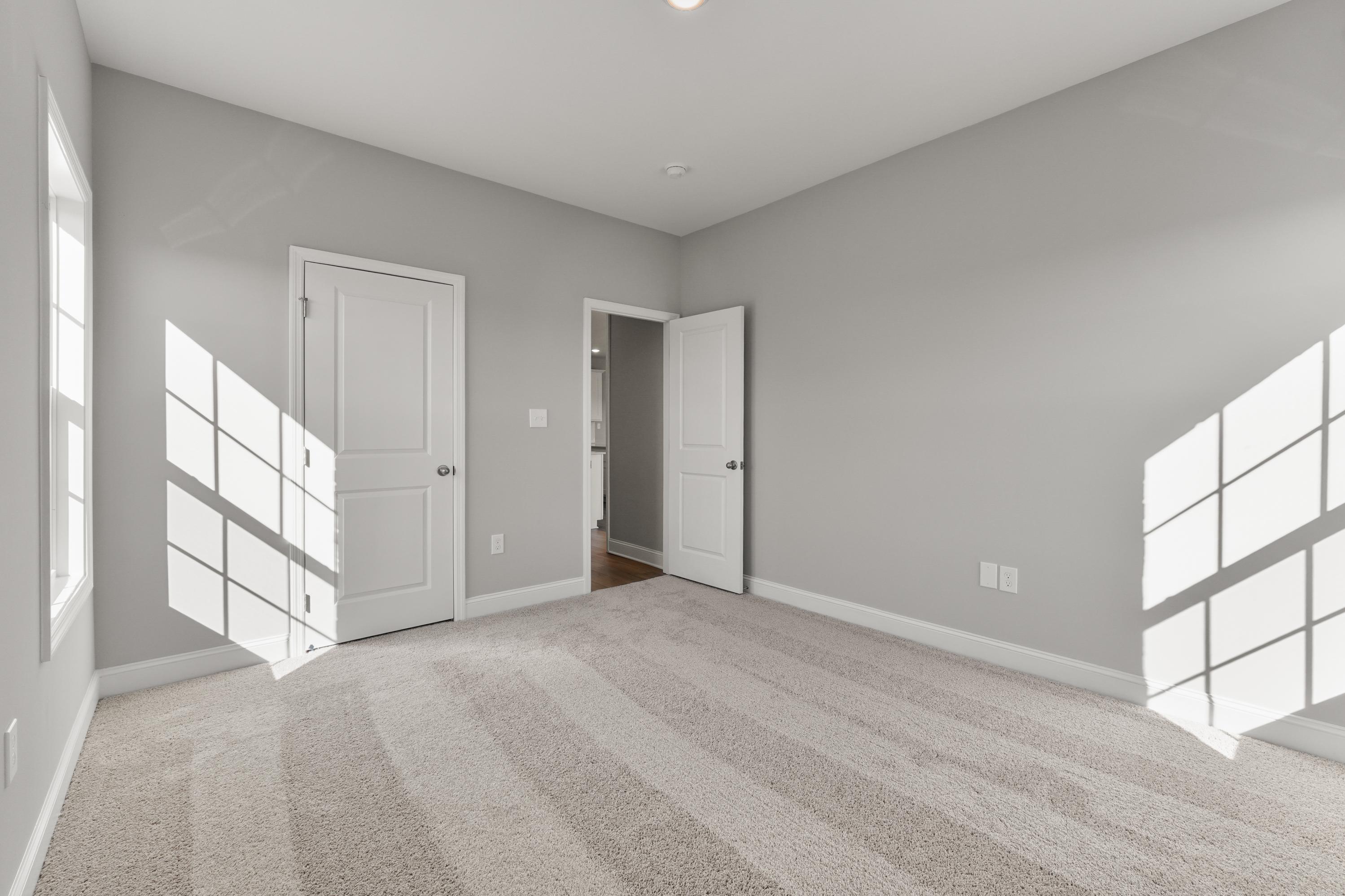 Spacious bedroom in The Valencia home with gray walls, beige carpet, white doors, and sunlit windows