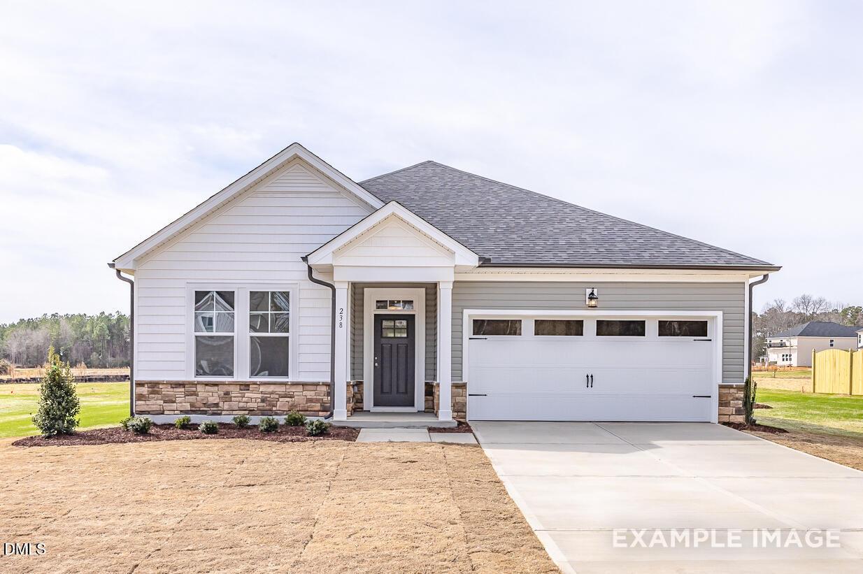 Charming 1-story 4-bedroom home exterior with 2-car garage, white siding, and brick accents in Woodland Crossing, Zebulon, NC