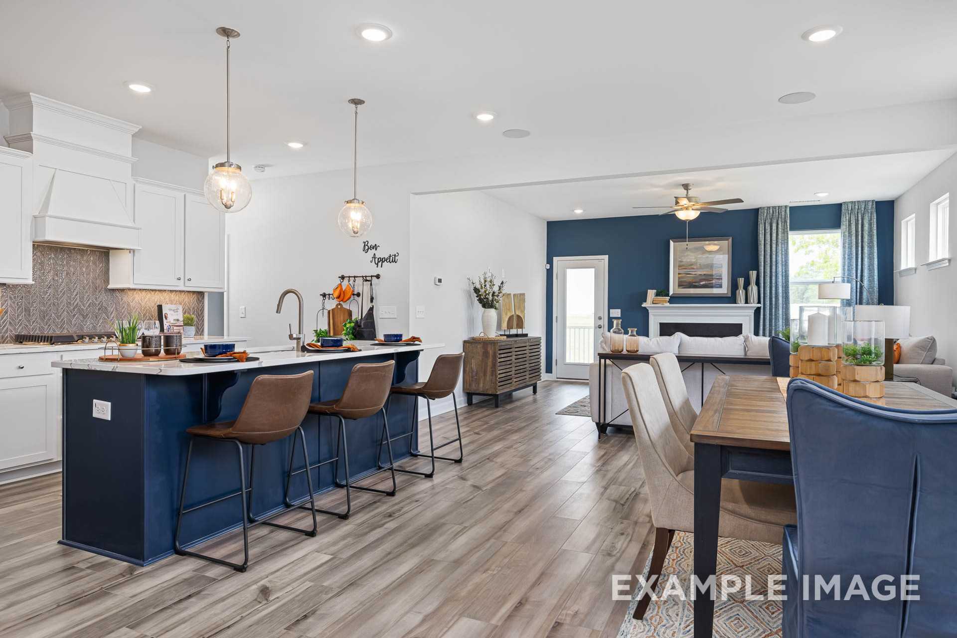 Spacious open-concept kitchen and dining in The Adalynn A with navy island, white cabinets, hardwood floors, and pendant lights
