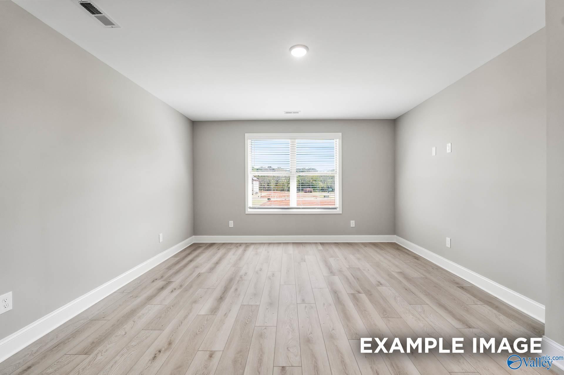 Spacious empty bedroom with light gray walls, oak laminate floors, and large window in Davidson Homes Everett B, Toney, Alabama