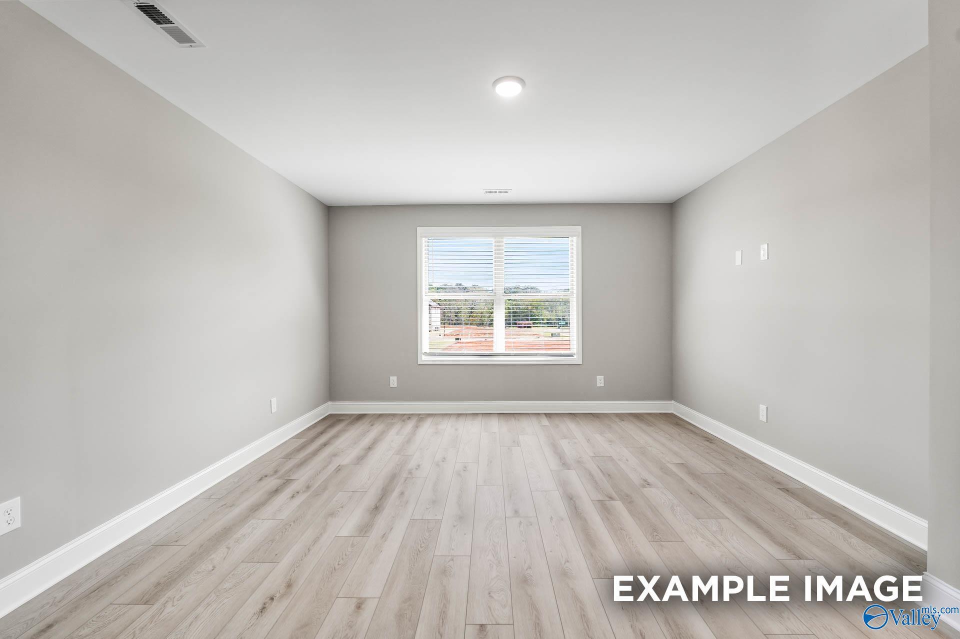 Spacious empty bedroom with light gray walls, oak laminate floors, and large window in Davidson Homes Everett B, Toney, Alabama