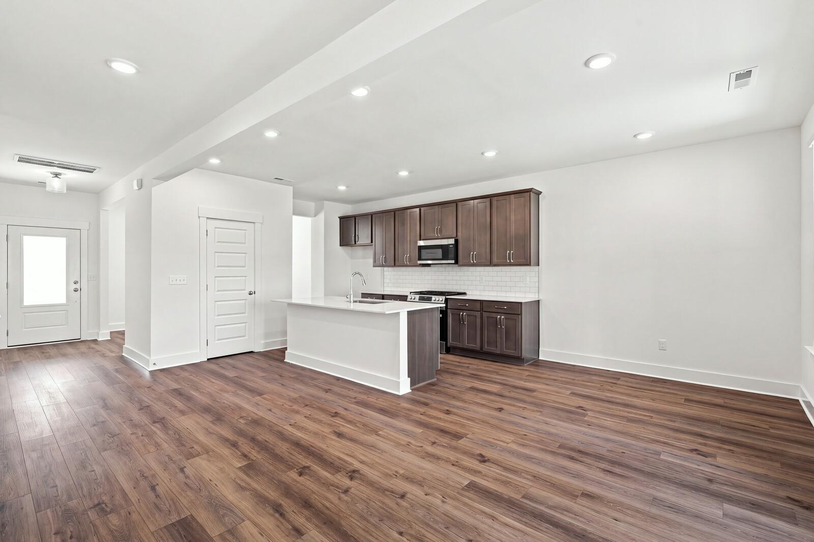 Open-concept kitchen with white island, dark cabinets, and luxury vinyl plank flooring in Davidson Homes Willow C, Gallatin TN
