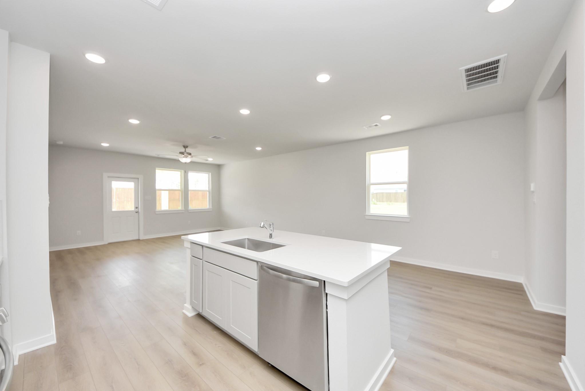 Open-concept kitchen island with stainless steel dishwasher in The Blanco F floor plan at Spring Branch Crossing, Conroe.