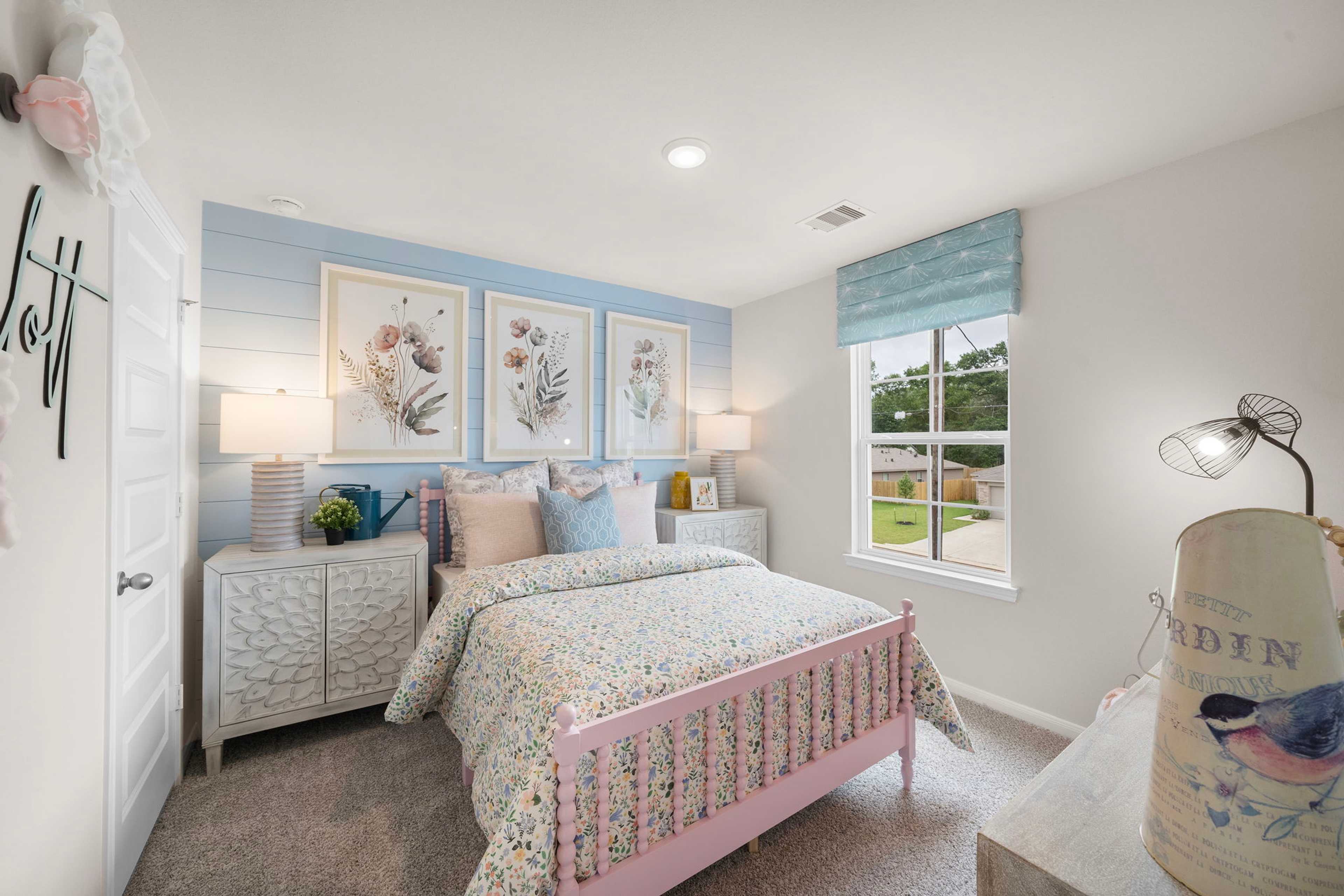 Charming girl's bedroom at Hill & Dale Ranch in Splendora Texas with pink floral bed, blue accent wall, and framed botanicals