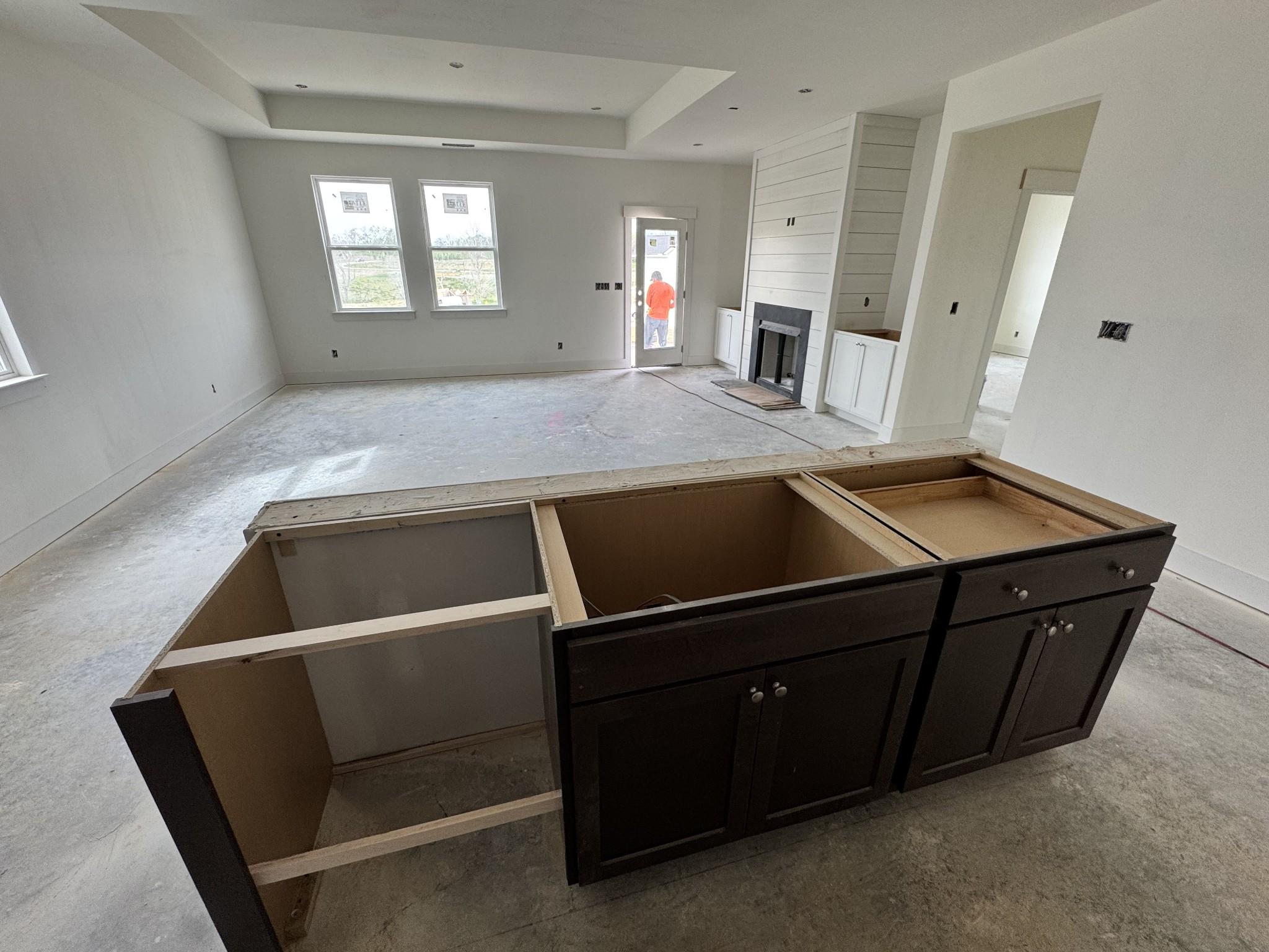 Under-construction open-concept kitchen with dark wood cabinets, stone fireplace, and large windows in Davidson Homes Cottonwood E, Gallatin TN