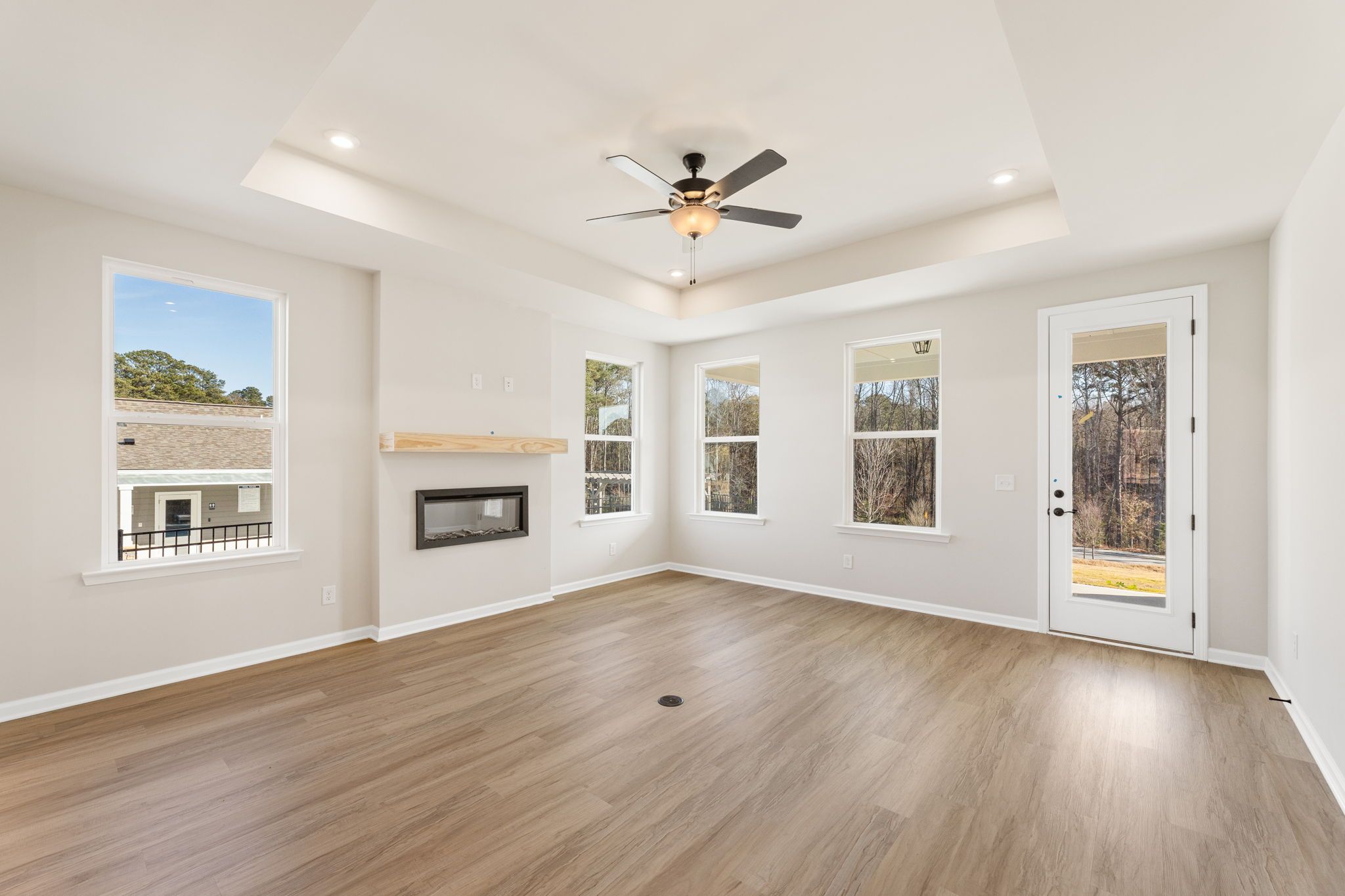 Bright living room with linear fireplace, wood floors, ceiling fan, and large windows in The Glenwood C by Davidson Homes, Loganville, GA