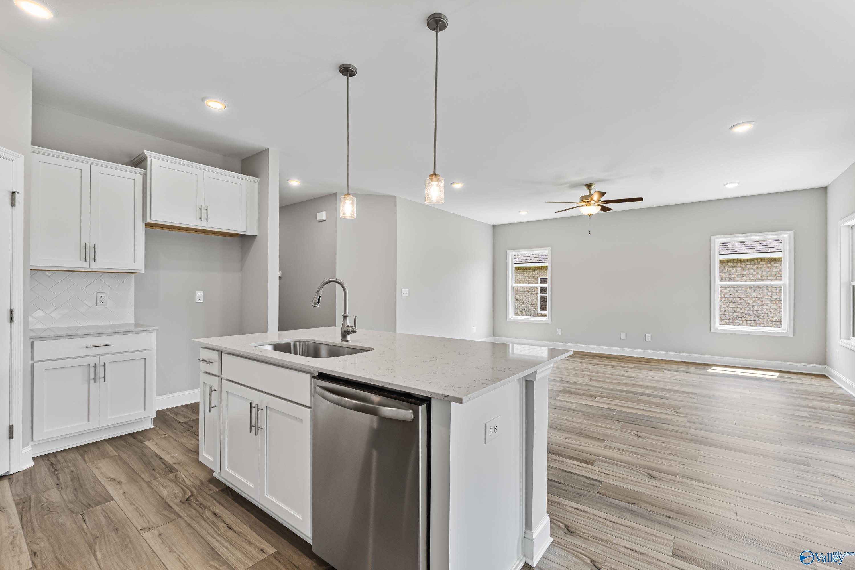 Modern white kitchen with quartz island, stainless dishwasher, hardwood floors in Davidson Homes The Franklin C, Huntsville AL