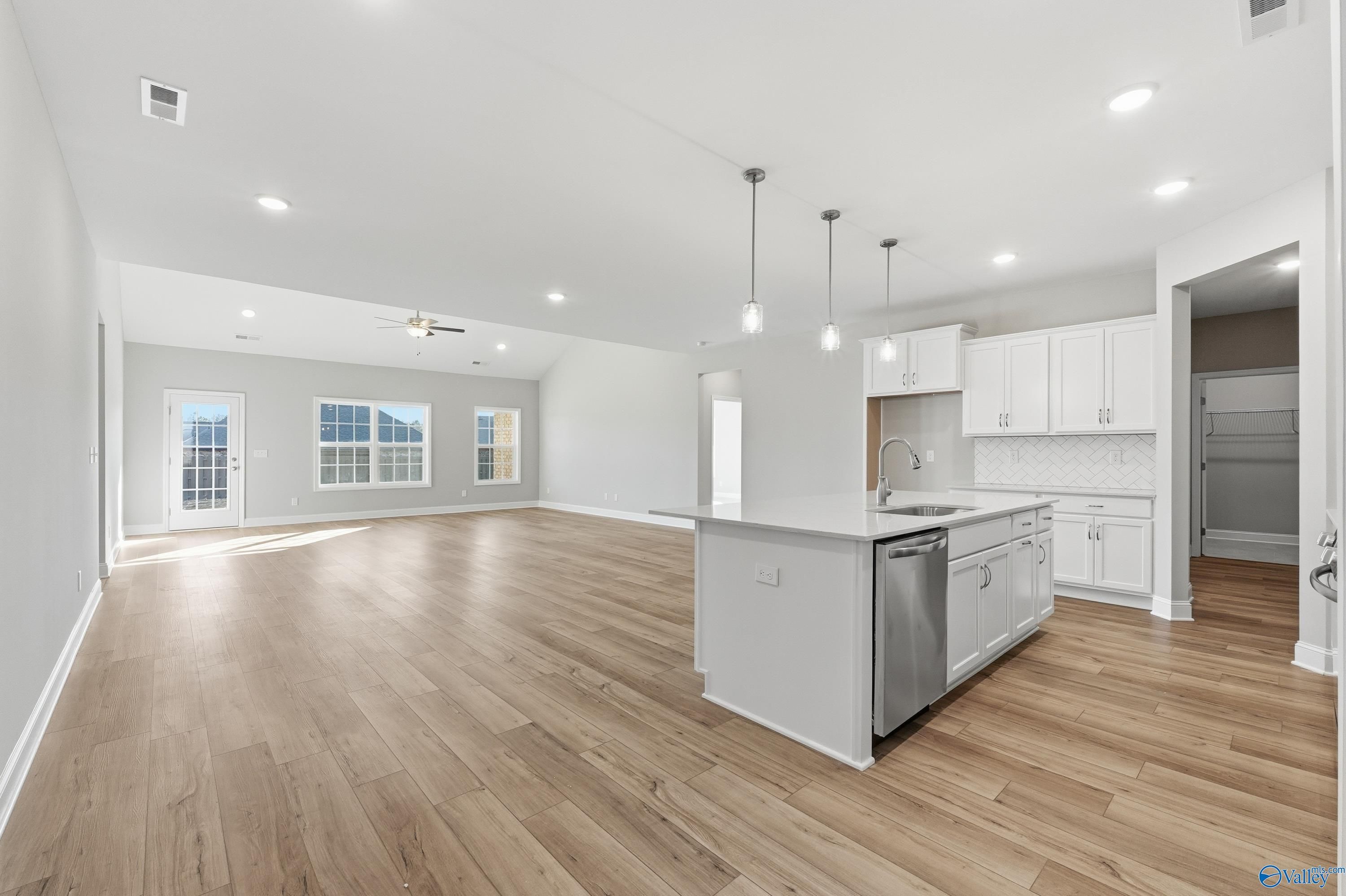 Open-concept kitchen with white cabinets, center island, stainless appliances and hardwood floors in The Lanier, Toney, Alabama
