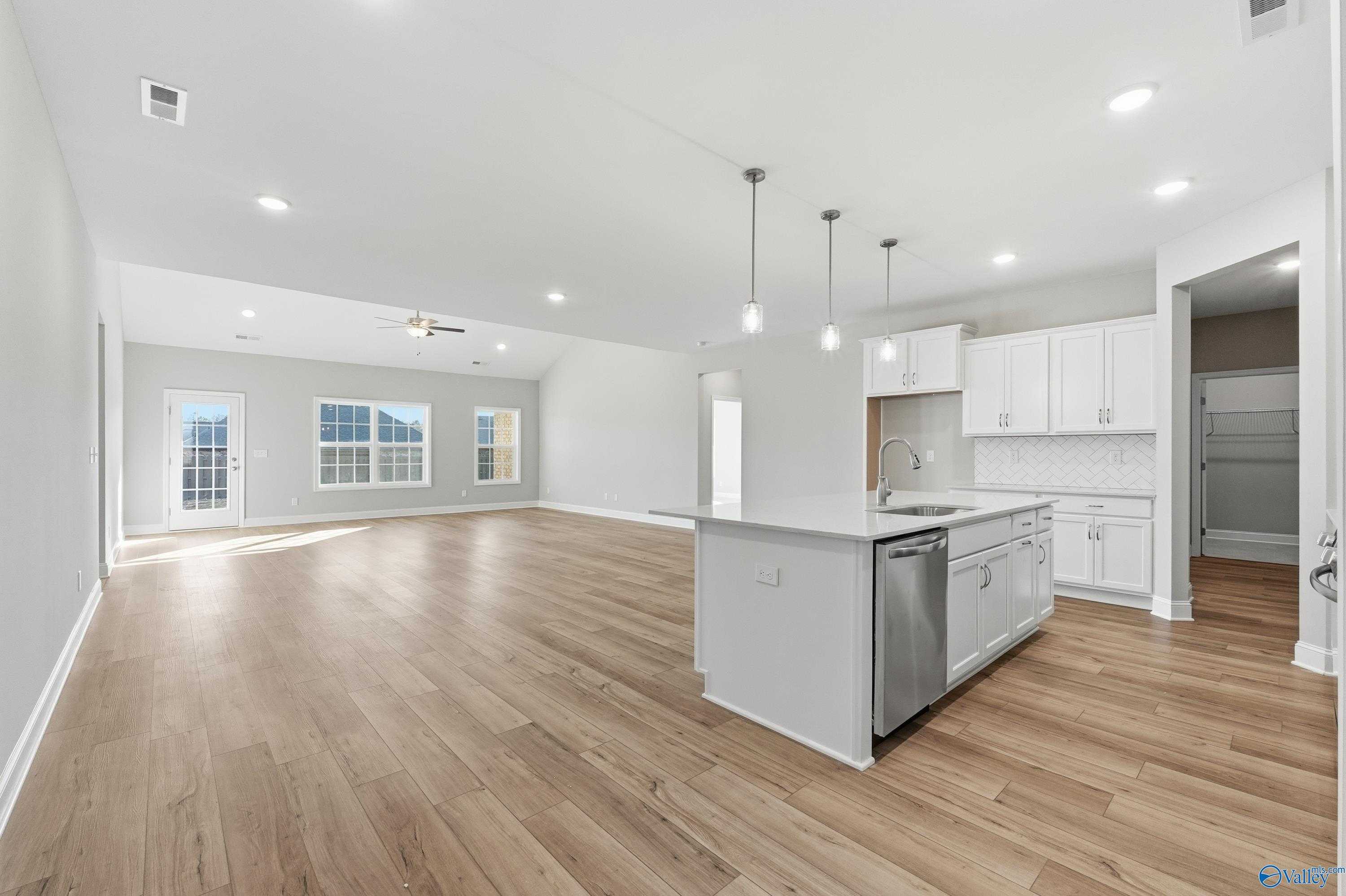 Open-concept kitchen with white cabinets, center island, stainless appliances and hardwood floors in The Lanier, Toney, Alabama