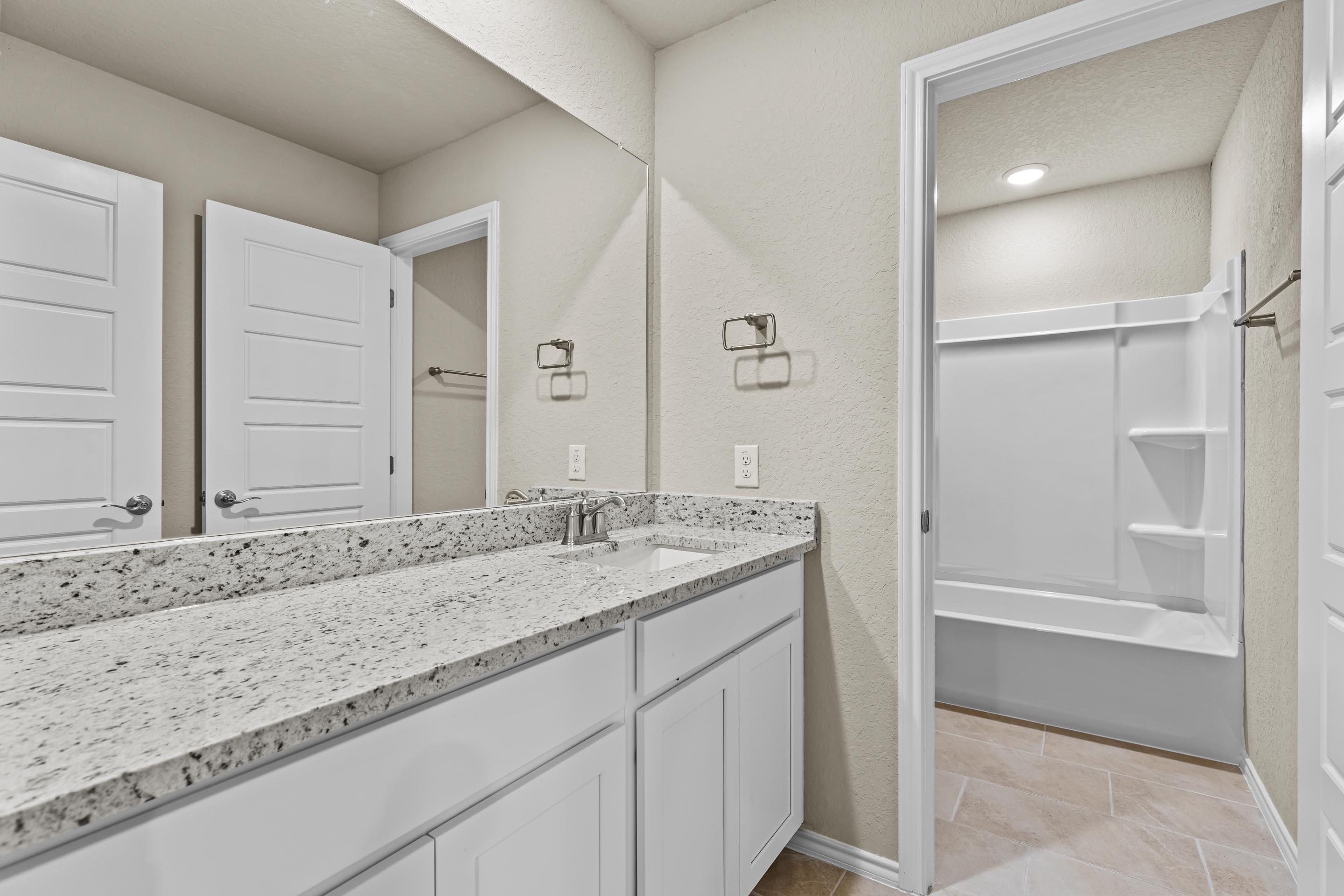 Modern master bathroom with double vanity, granite counters, glass shower, and tub in Davidson Homes The Douglas F, San Antonio