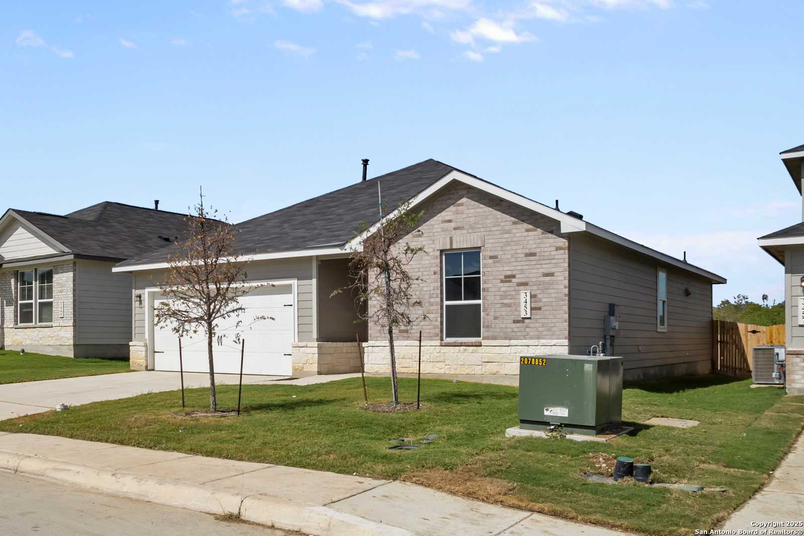 Single-story gray brick home with 2-car garage, young trees, and grassy yard in Horizon Pointe, Converse, Texas - Davidson Homes Asheville H