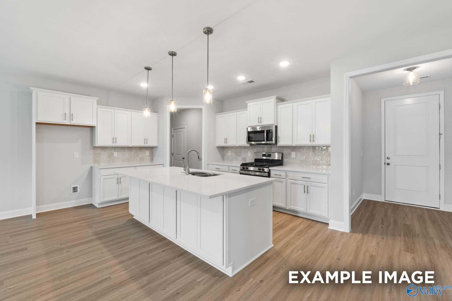 Modern white kitchen with large island, stainless appliances, pendant lights in Davidson Homes The Lanier, Meridianville, AL