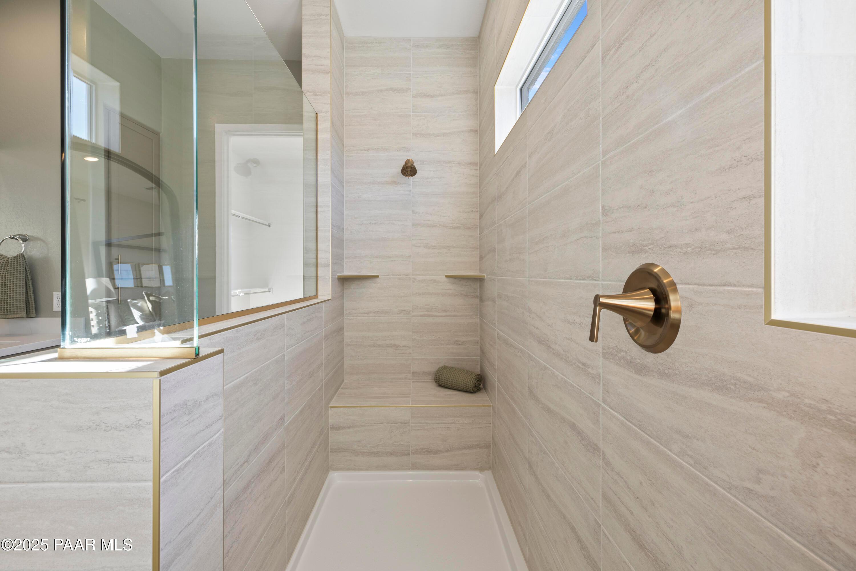 Modern walk-in shower with frameless glass enclosure, beige porcelain tiles, bronze fixtures in The Blaze D master bath, Prescott AZ