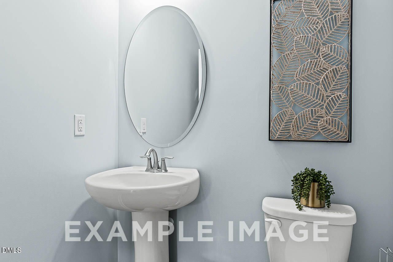 Elegant powder room with white pedestal sink, oval mirror, and decorative leaf wall art in Davidson Homes The Ash C plan, Lillington NC