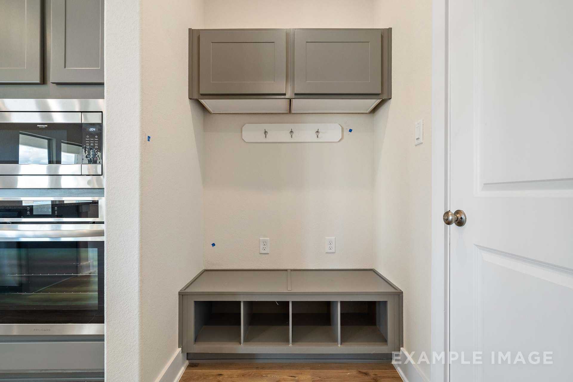 The Diana C mudroom featuring gray built-in bench with storage, wall hooks, and adjacent stainless steel appliances