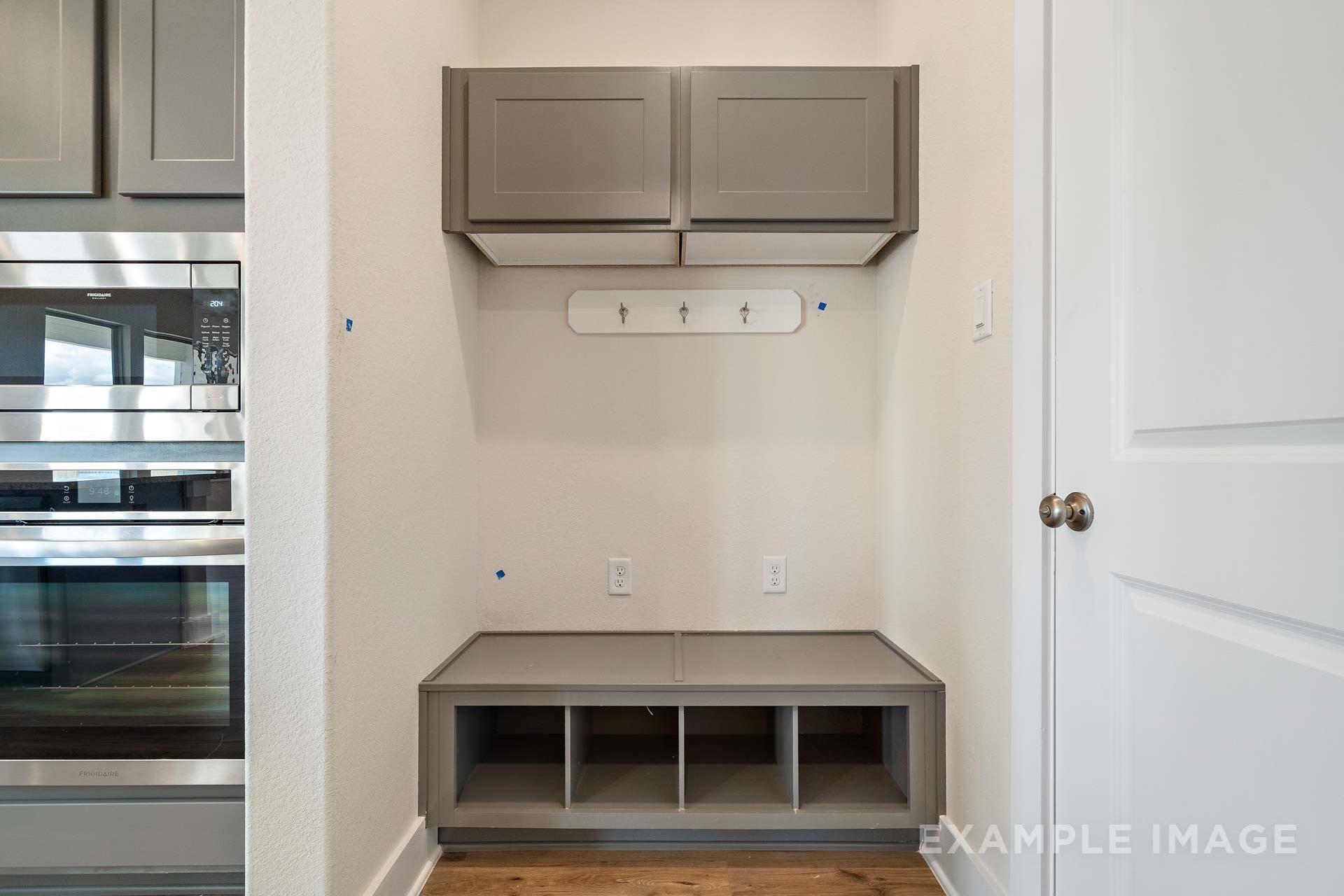 The Diana C mudroom featuring gray built-in bench with storage, wall hooks, and adjacent stainless steel appliances