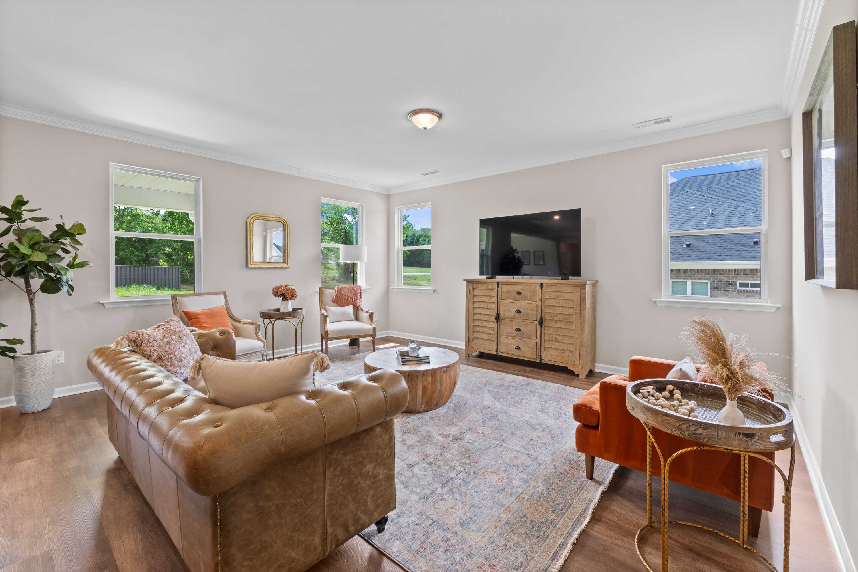 Spacious living room at Riverton Preserve in Huntsville Alabama with leather sofa, wooden accents, large windows, and neutral decor