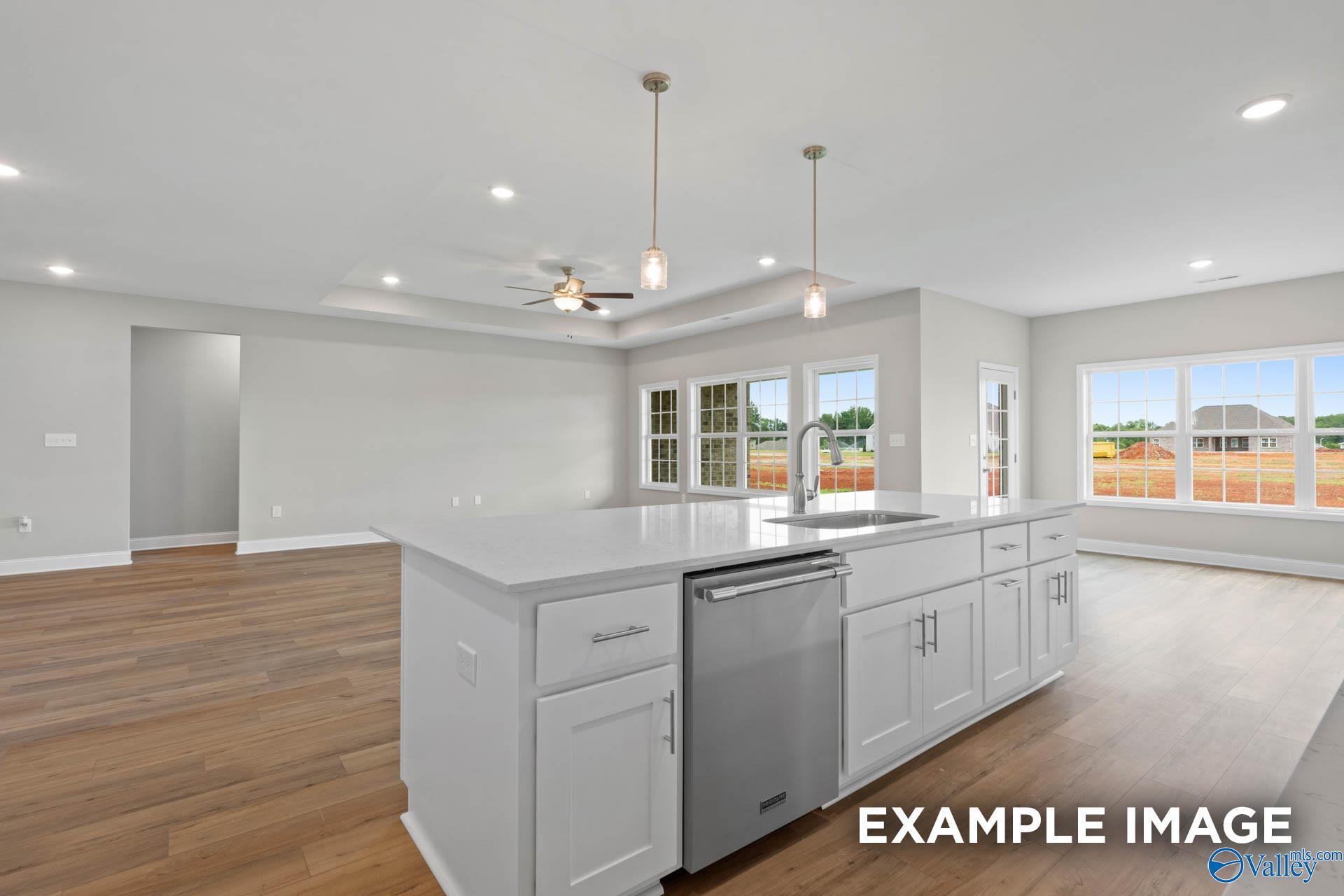 Modern open-concept kitchen with white island, stainless dishwasher, hardwood floors, and large windows in Davidson Homes The Finleigh, Harvest, AL