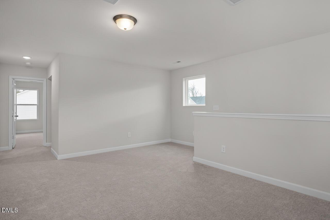 Spacious upstairs loft with light gray walls, beige carpet, and window in Davidson Homes The Gavin B, Gregory Village, Lillington NC